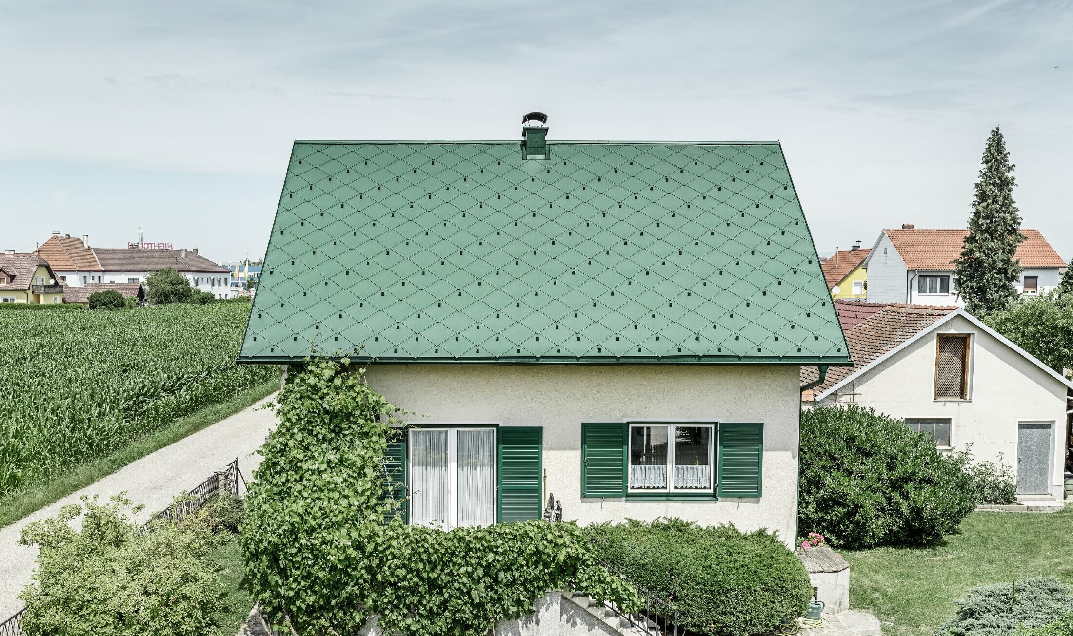 Klasický rodinný dom so sedlovou strechou so strešnou krytinou z hliníka vo farbe machovozelená so zelenými okenicami. Strecha bola pokrytá PREFA strešnými šablónami 44 × 44 vo farbe P.10 machovozelená.