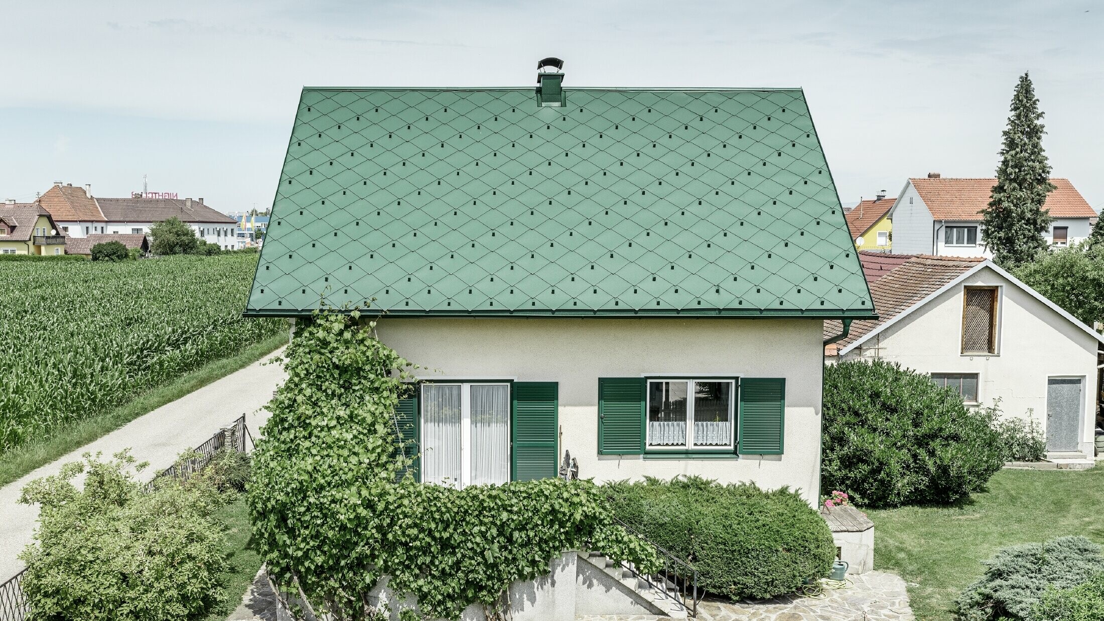 Klasický rodinný dom so sedlovou strechou so strešnou krytinou z hliníka vo farbe machovozelená so zelenými okenicami. Strecha bola pokrytá PREFA strešnými šablónami 44 × 44 vo farbe P.10 machovozelená.