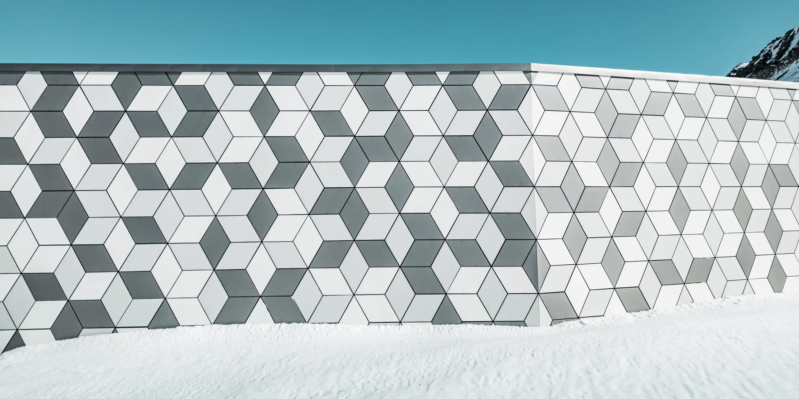 Detailný záber na fasádu stanice lanovky Jandri v Les Deux Alpes ukazuje presné usporiadanie diamantov z hliníkových kompozitných panelov PREFABOND. Diamanty sú usporiadané do pútavého vzoru. Vďaka harmonickej farebnej schéme v rôznych odtieňoch bielej a sivej farby fasáda dokonale ladí so zasneženou alpskou krajinou. Robustné panely odolné voči poveternostným vplyvom sú odolným a estetickým riešením pre extrémne poveternostné podmienky v horách.