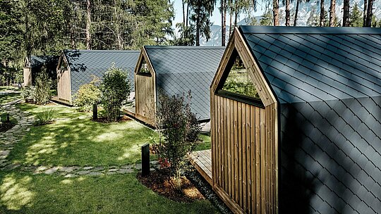 Rad minimalistických minidomov Secret Koi Garden sa rozprestiera uprostred udržiavanej zelene pri jazere Natterer See. Šikmé strechy a fasády sú vyhotovené z malých hliníkových šablón PREFA v odtieni P.10 antracit, ktoré vytvárajú pokojnú štruktúru pripomínajúcu rybiu kožu. Obklopené stromami a kríkmi poskytujú odolné a poveternostne odolné hliníkové povrchy PREFA optimálnu ochranu a dodávajú glampingovému rezortu jasný, nadčasový architektonický jazyk v súlade s prírodou.