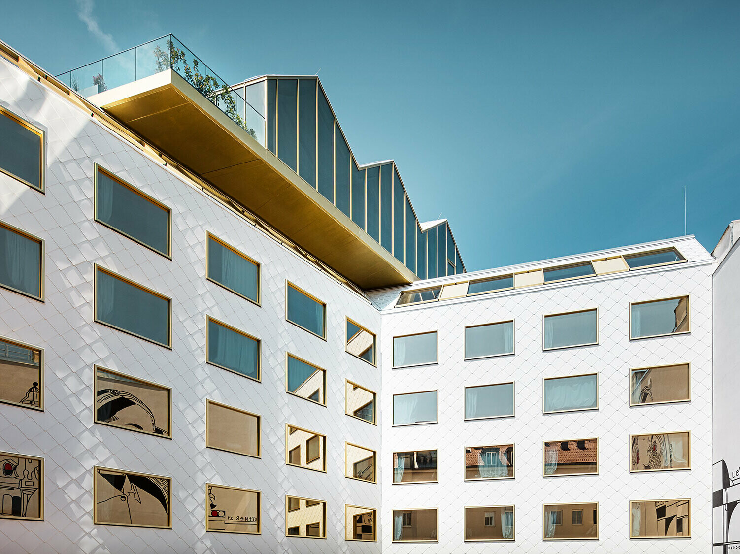 Blick auf das Hotel vom Innenhof aus; ein Wandkunstwerk spiegelt sich in den Fenstern, die Rooftop Bar kragt leicht über dem Hotel aus.