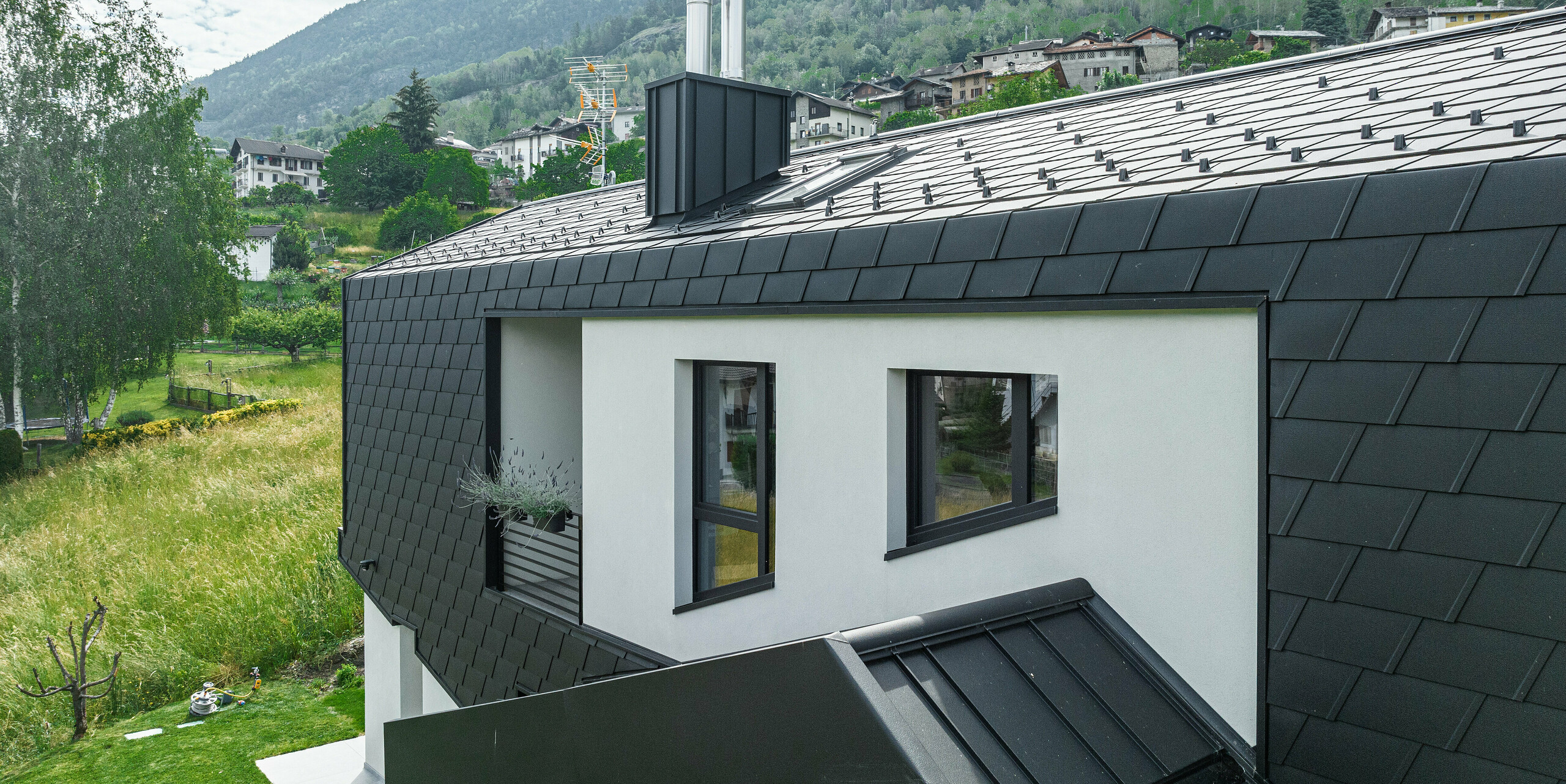 Pohľad na horné poschodie nehnuteľnosti "Zaffhaus" v Taliansku. Dom má strechu a fasádu z čiernych šindľov PREFA. Rodinný dom sa vyznačuje geometrickou presnosťou a moderným dizajnom. Hliníkové šindle dodávajú stavbe štruktúrovanú hĺbku, zatiaľ čo elegantne integrované okná a komín podčiarkujú estetický a funkčný dizajn.