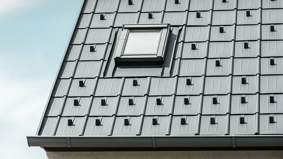 PREFA Dachplatte mit Schneestoppern in Anthrazit verlegt mit eingebautem Dachfenster und PREFA Dachrinne. Dachfläche mit PREFA Blechdach