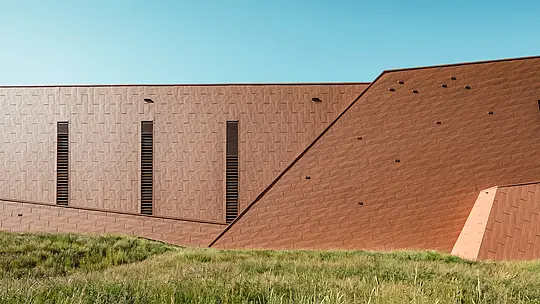 Čerpacia stanica pitnej vody v Lottume (Holandsko) sa ako sochársky architektonický celok harmonicky začleňuje do prírodného prostredia. Výrazná hliníková fasáda PREFA Siding.X v teplom vzhľade hrdze vytvára zaujímavý kontrast so zelenou lúkou a kopcami a fascinuje svojím jemne štruktúrovaným, živým povrchom. Štíhle, vertikálne otvory vytvárajú precízne akcenty. Odolné, ľahké a úplne recyklovateľné hliníkové panely PREFA presviedčajú vysokou odolnosťou voči poveternostným vplyvom, stálosťou farieb a udržateľným plášťom budovy, ktorý nevyžaduje náročnú údržbu. Vďaka tomu je čerpacia stanica pitnej vody architektonickým lákadlom v oblasti infraštruktúry.