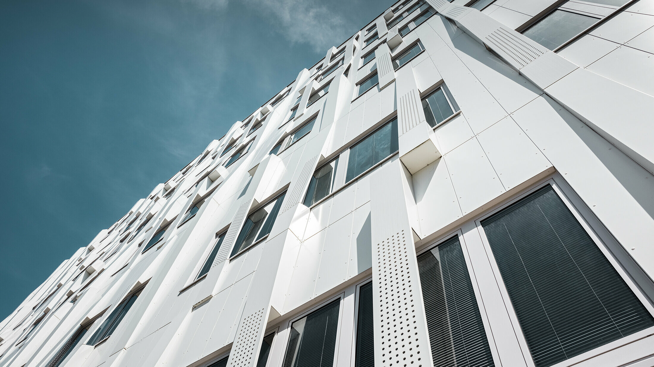Nahaufnahme der 3D-Fassade mit gelochten Aluminium Verbundplatten-Kassetten und normalen PREFA Verbundplatten in Reinweiß. Die Kassettenfassade von PREFA macht das Gebäude zu einem Blickfang.