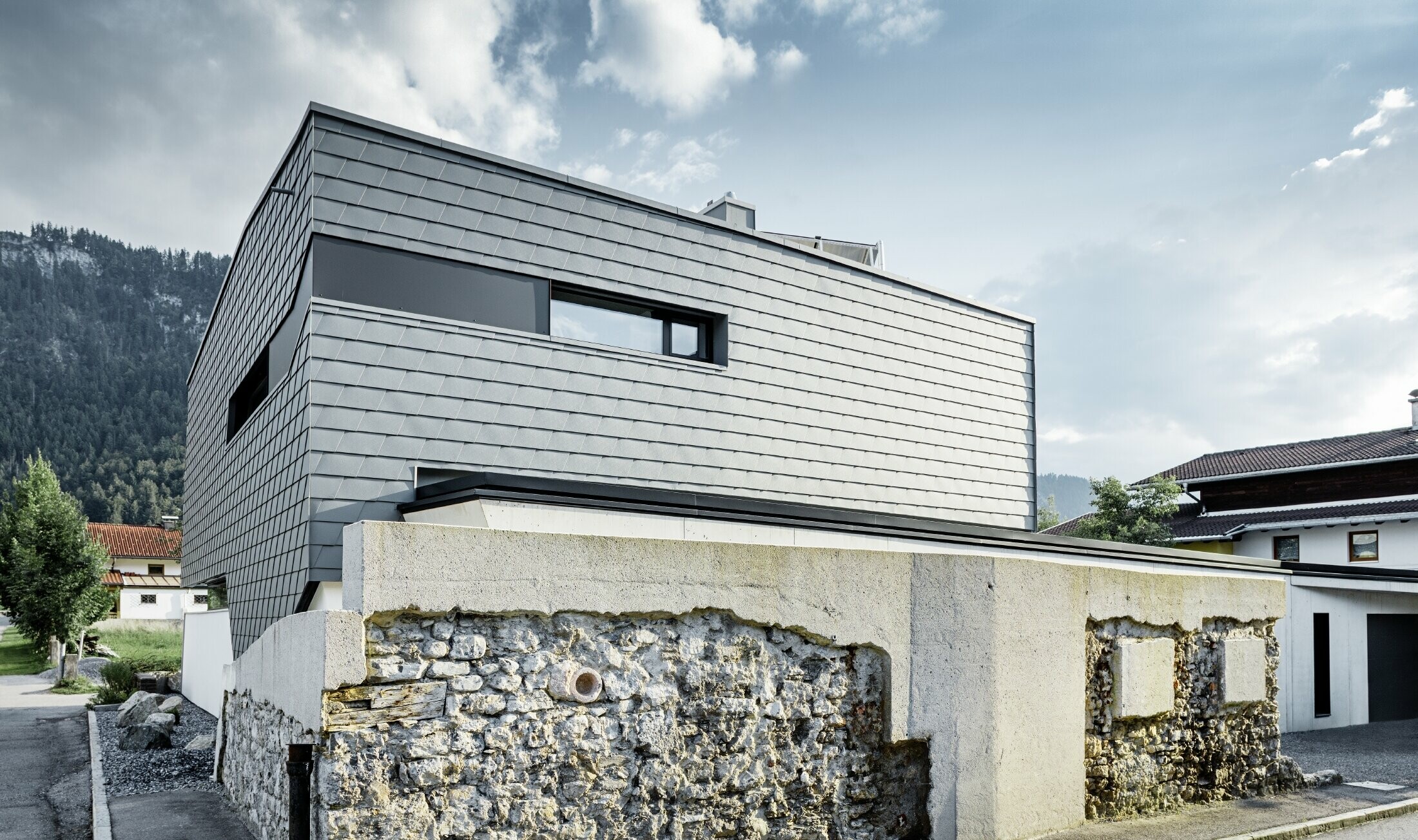 Moderný rodinný dom s plochou strechou, veľkými oknami a šindľovou fasádou v svetlošedom hliníku od firmy PREFA