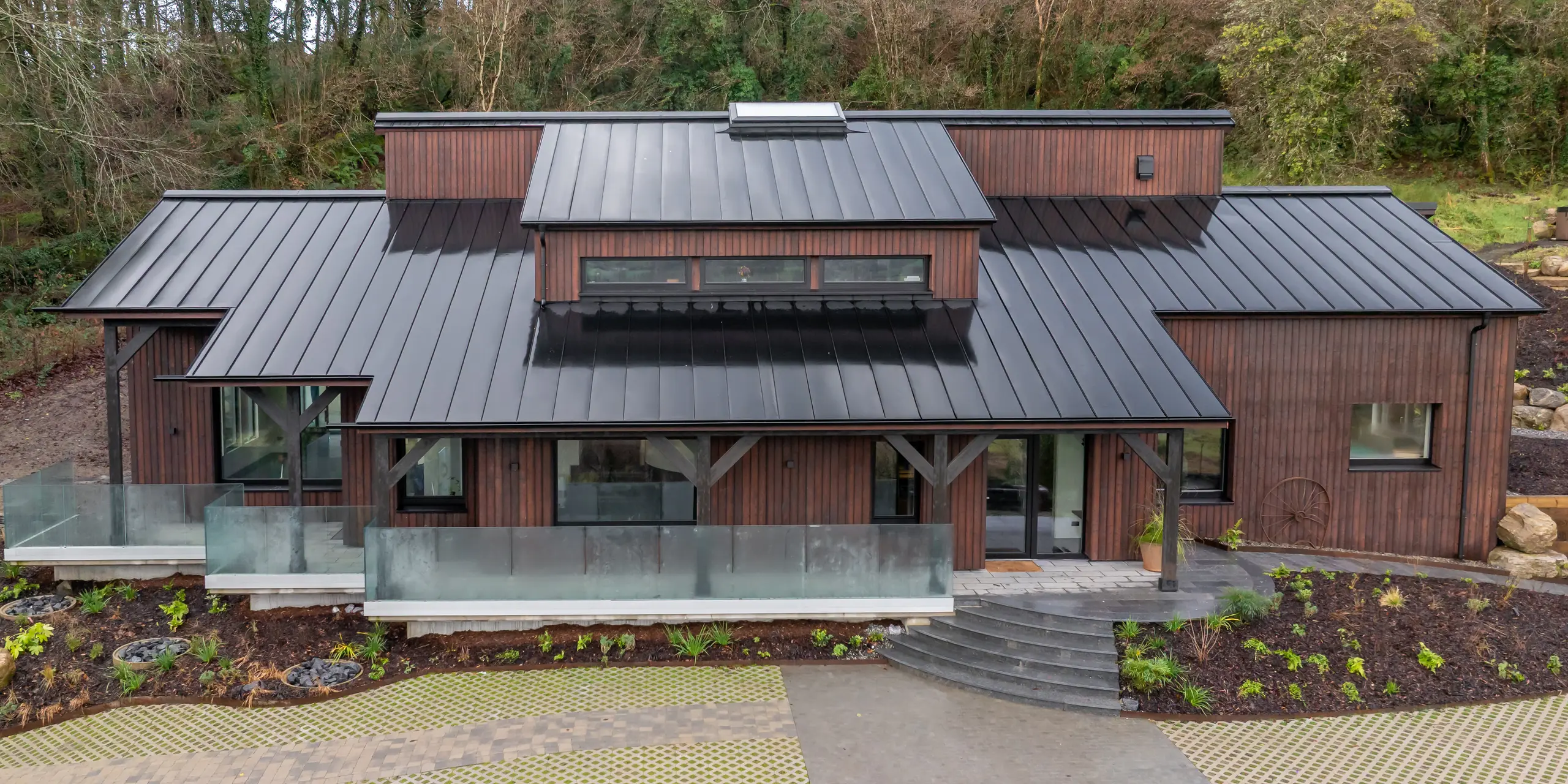 Modernes Einfamilienhaus in Sligo, Irland, eingebettet in eine natürliche Hanglage, mit markanter Holzfassade und beeindruckendem PREFALZ Aluminiumdach in P.10 Schwarz. Die klar strukturierte Stehfalzdeckung zieht sich dynamisch über mehrere Dachflächen und setzt einen starken architektonischen Akzent. Großzügige Glasfronten, Terrassenbereiche und präzise Linienführung unterstreichen das Design. Das PREFA Aluminiumdach überzeugt durch Langlebigkeit, Korrosionsbeständigkeit und hohe Widerstandsfähigkeit gegenüber den wechselhaften Wetterbedingungen.