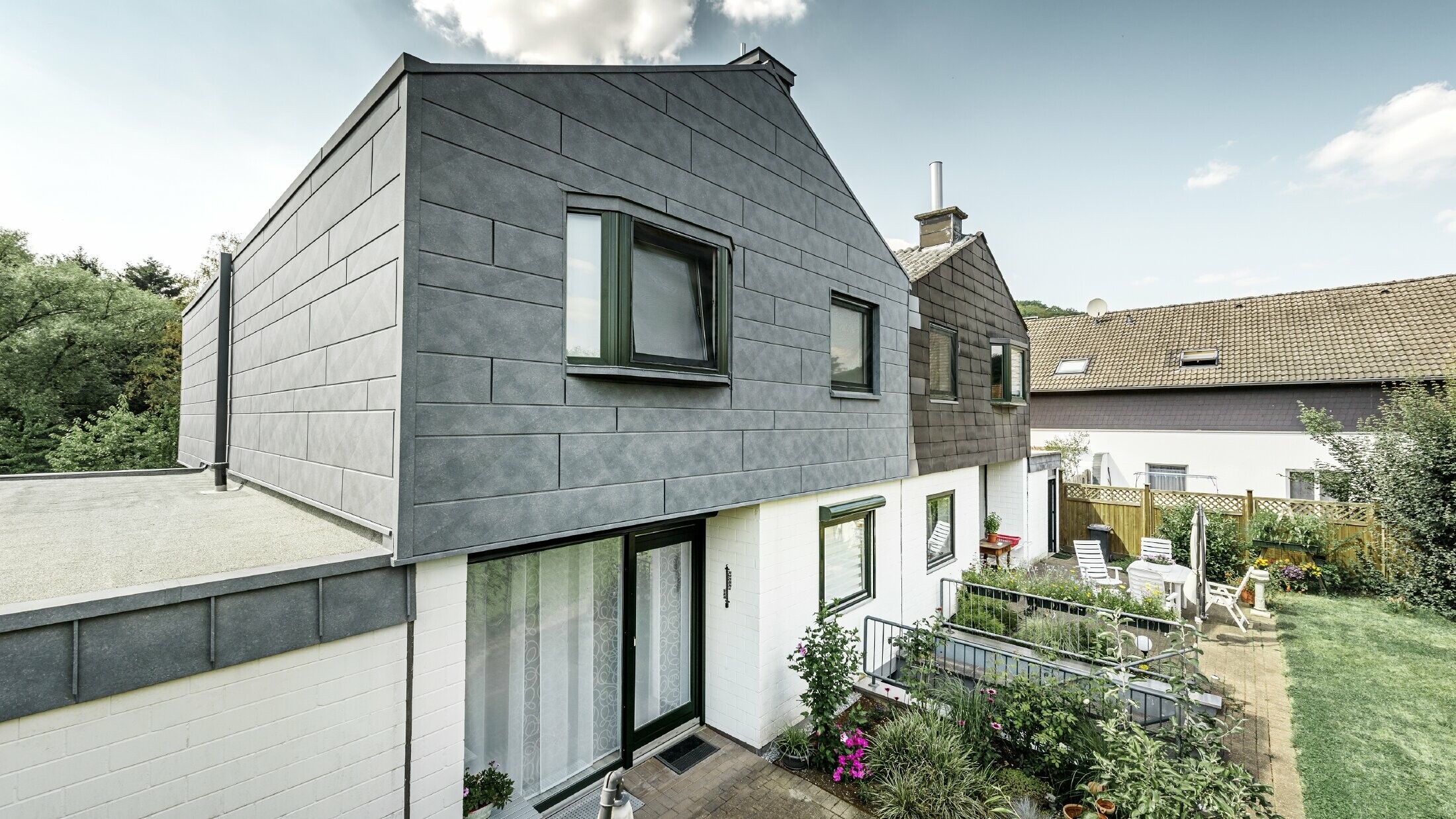 Vrchná časť dvojposchodového domu bola zrekonštruovaná s PREFA fasádnym prvkom Siding.X v odtieni kamenná šedá P.10. Vedľa stojí polovička domu pred rekonštrukciou.    