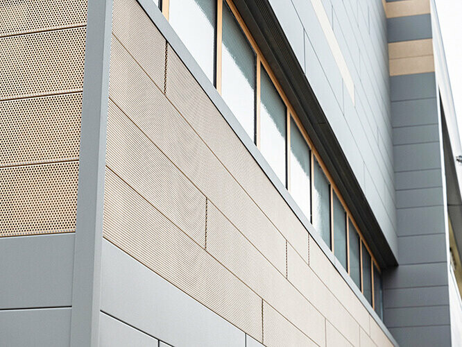 Fasádne panely PREFA Siding sú tiež dostupné v perforovanom, ako aj dierovanom vyhotovení, tu sú pieskovo hnedé dierované prvky kombinované so sivými panelmi. 