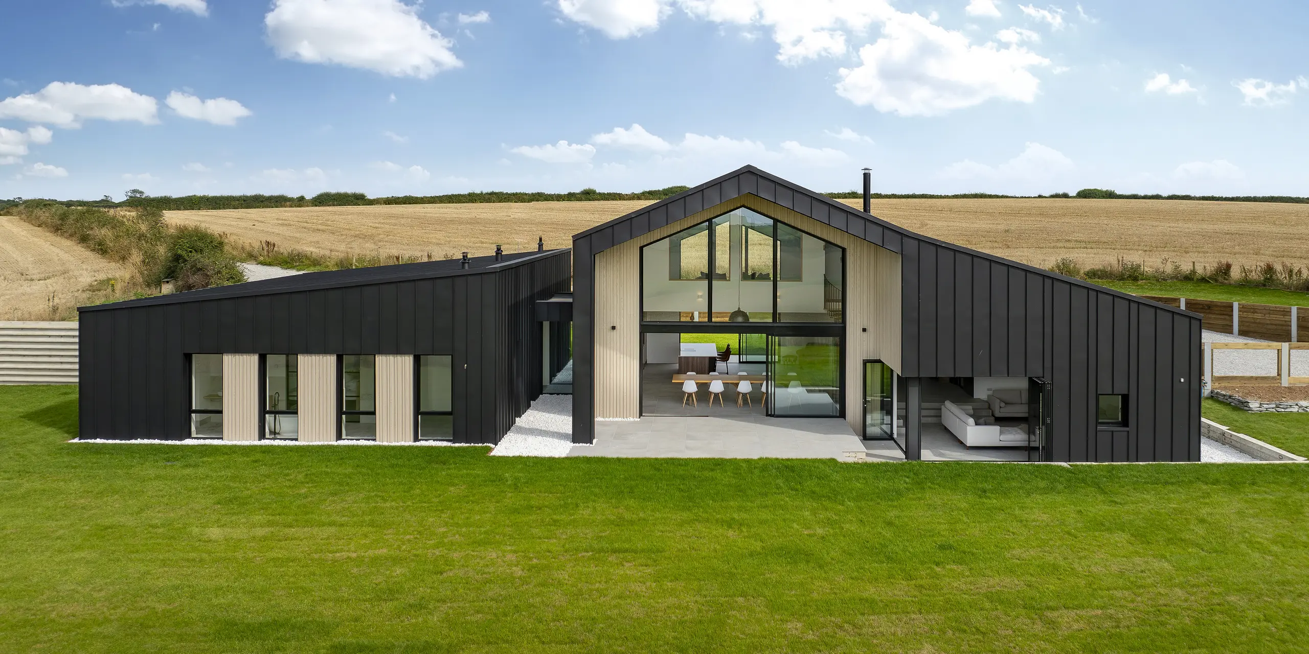 Frontale Ansicht auf die Rückseite von ‚The Hide‘ in Cornwall. Die großzügige Glasfassade, eingerahmt von einer PREFALZ Aluminiumverkleidung in P.10 Anthrazit, öffnet den Innenraum zum weitläufigen Garten. Die klare Stehfalzoptik in Kombination mit natürlichen Holzelementen unterstreicht das moderne und harmonische Design.