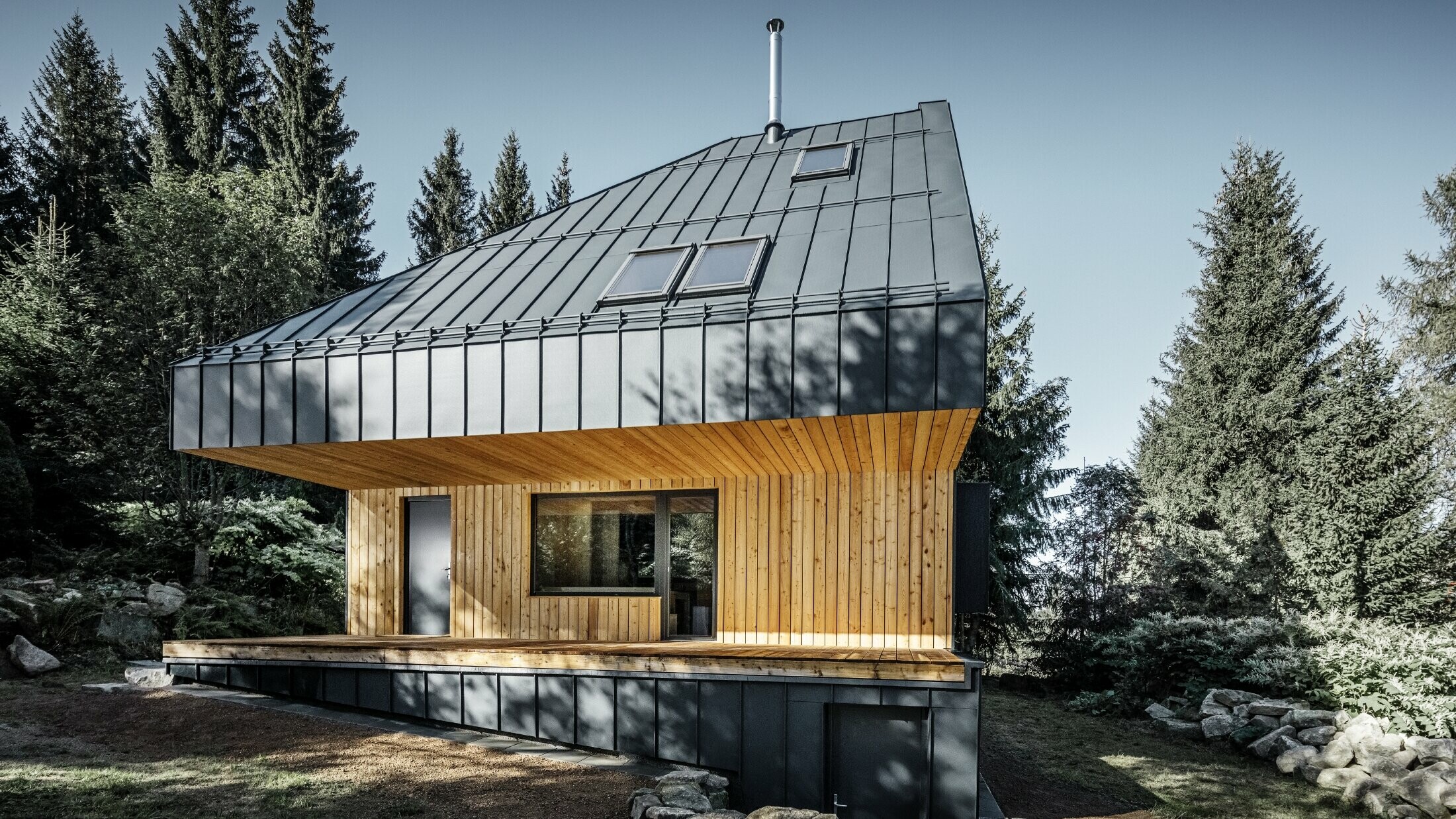 Architektonický rodinný dom v lese, impozantná strecha bola opláštená hliníkovým profilom PREFA Prefalz v antracitovej farbe. Podhľad a fasáda sú obložené drevenými panelmi.