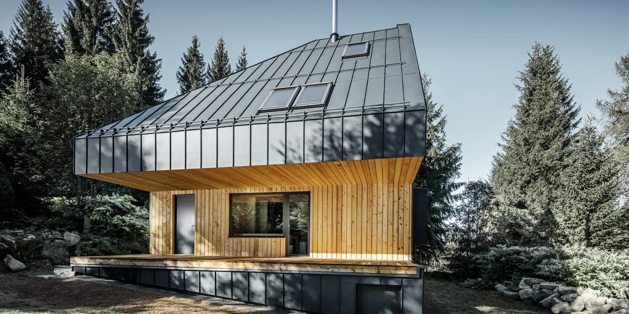 Architektonický rodinný dom v lese, impozantná strecha bola opláštená hliníkovým profilom PREFA Prefalz v antracitovej farbe. Podhľad a fasáda sú obložené drevenými panelmi.