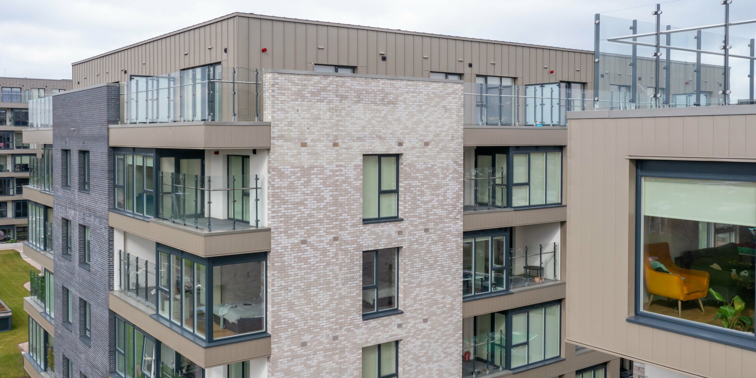 Záber z dronu na obytný komplex Palmers Gate v Palmerstowne, Dublin, Írsko. Komplex budov pozostáva z niekoľkých obytných blokov s obkladmi PREFA Siding v bronzovej farbe a fasádnym systémom PREFALZ. Fasáda kombinuje vysokokvalitný plechový obklad s tehlovými prvkami a veľkými sklenenými oknami. Vonkajšie priestory sú navrhnuté so zelenými plochami, chodníkmi a kvetináčmi, ktoré poskytujú príjemné prostredie pre obyvateľov. Celkovo sa použilo približne 1 700 m² PREFA Siding a približne 1 200 m² fasádneho systému PREFALZ. Hliníkové výrobky sú známe svojou odolnosťou a estetickým vzhľadom.