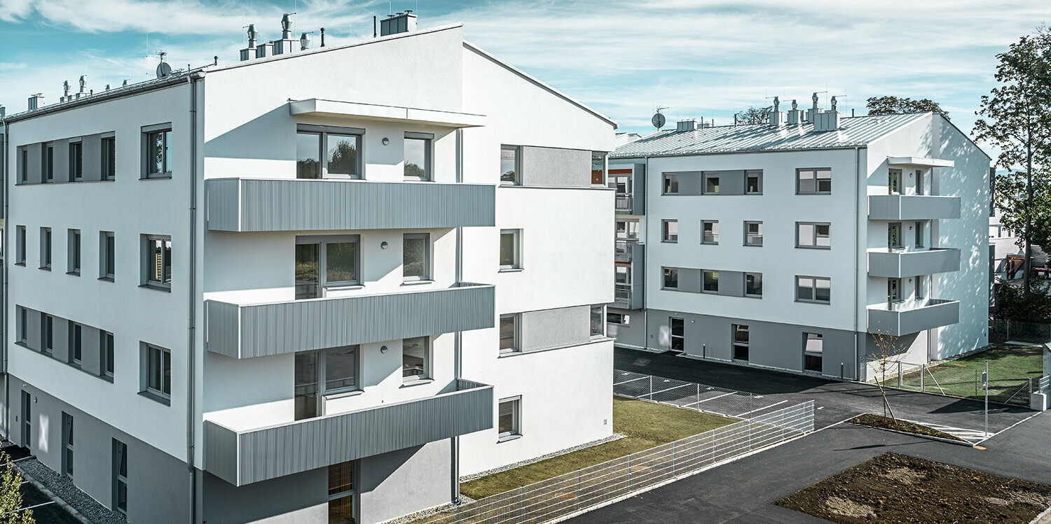 Moderný bytový dom s bielou fasádou a balkónmi s PREFA prelamovaným profilom vo farbe strieborná metalíza
