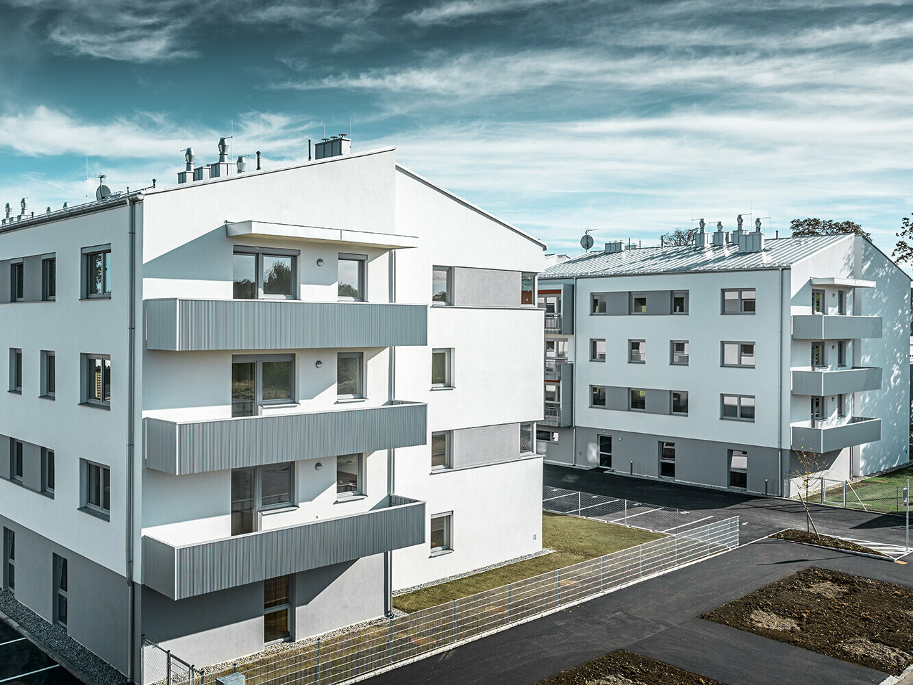 Moderný bytový dom s bielou fasádou a balkónmi s PREFA prelamovaným profilom vo farbe strieborná metalíza