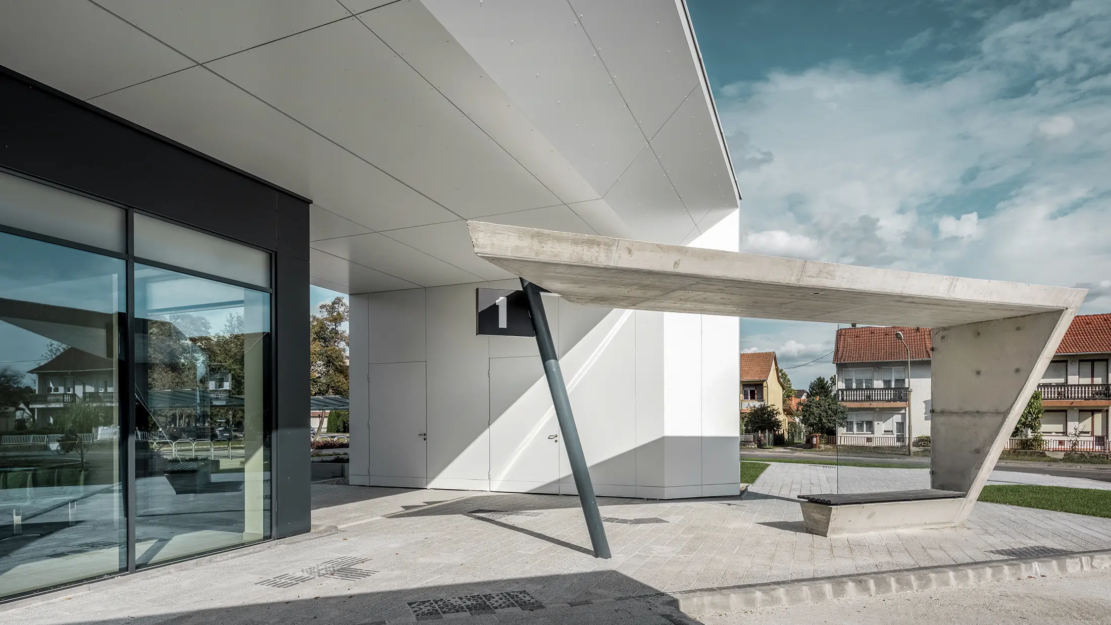 Vstupná časť autobusovej stanice Lenti; spodná strana strechy je obložená hliníkovým kompozitným panelom PREFABOND od spoločnosti PREFA v čiste bielej farbe, fasádne prvky pri vchodových dverách a výkladoch sú obložené v antracitovej farbe P.10.