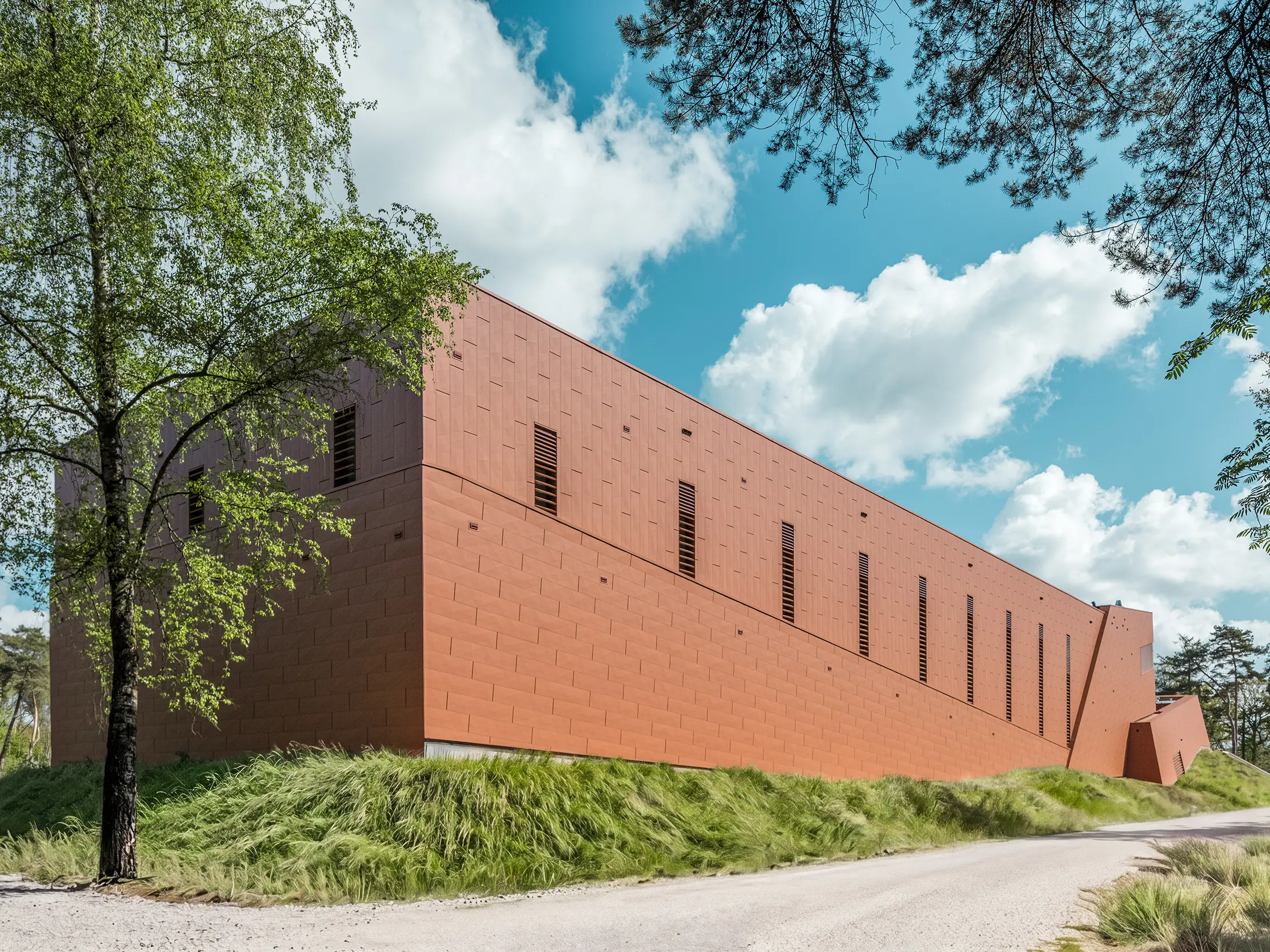 Podlhovastá čerpacia stanica pitnej vody WML v Lottume sa javí ako impozantná stavba uprostred prírodnej krajiny plnej stromov, lúk a panorámy oblohy. Výrazná hliníková fasáda PREFA Siding.X v teplom vzhľade hrdze priťahuje všetky pohľady ako vizuálny magnet a fascinuje svojím jemne fazetovaným povrchom s živou štruktúrou. Štíhle, vertikálne otvory rytmicky členia fasádu. Trvanlivé, ľahké a recyklovateľné hliníkové panely PREFA ponúkajú najvyššiu odolnosť voči poveternostným vplyvom, stálosť farieb a udržateľný plášť budovy s nízkymi nárokmi na údržbu.