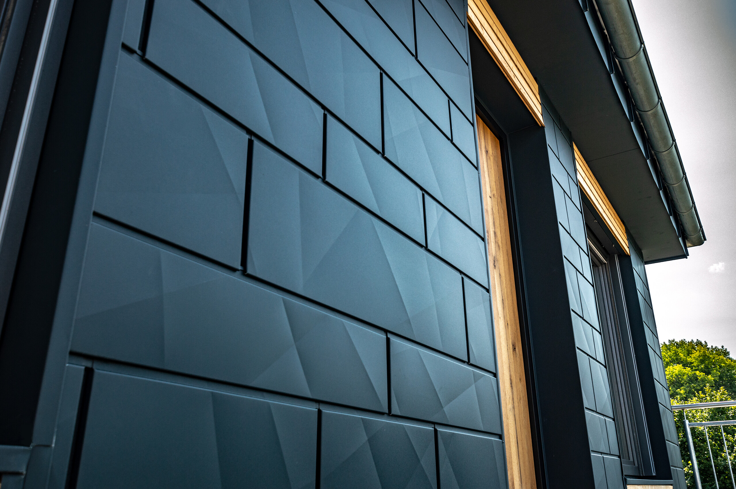 Fasáda s obkladom PREFA Siding.X v antracitovej farbe s balkónovými dverami a veľkými sklenenými plochami v kombinácii s drevenou fasádou.