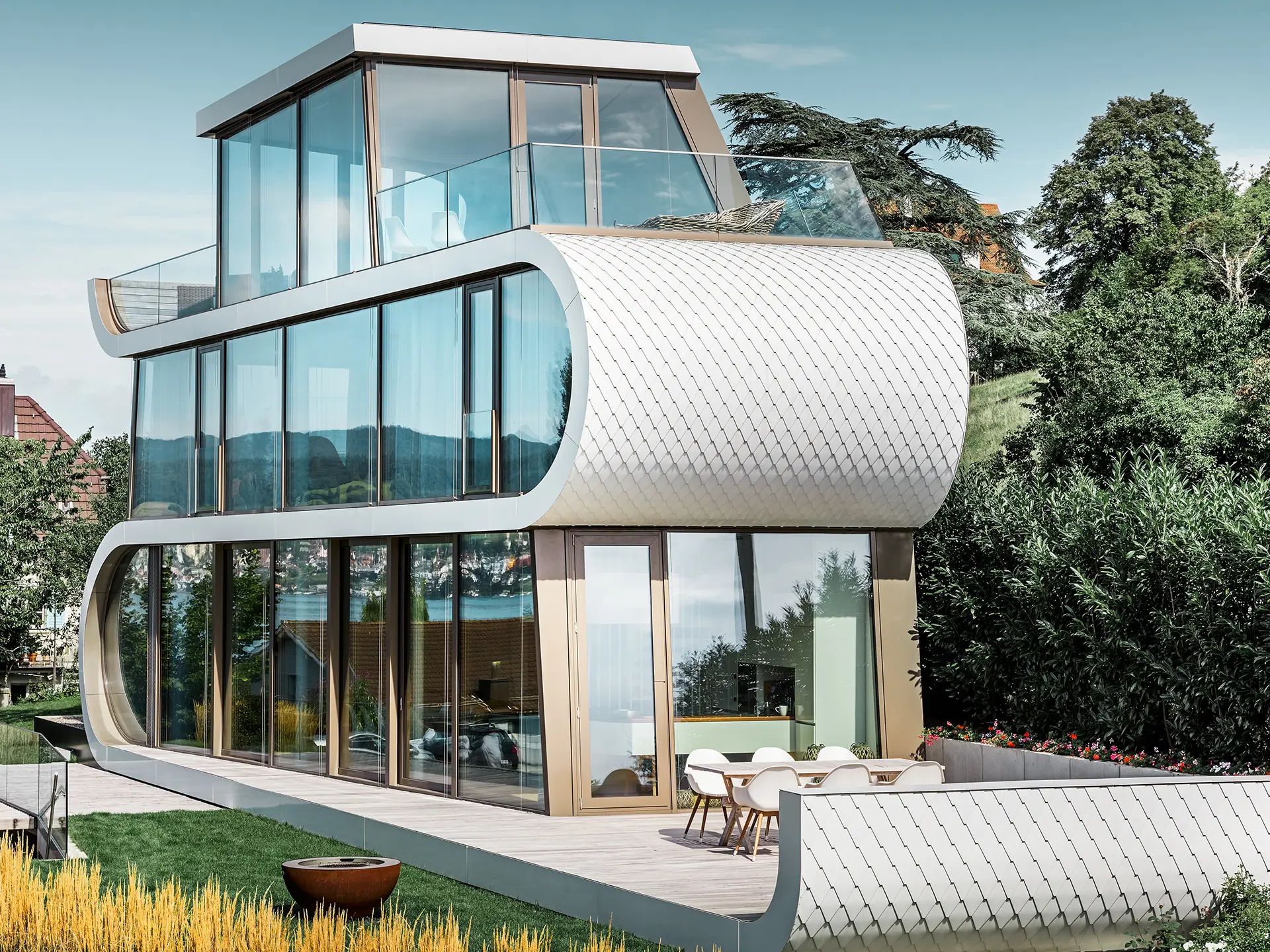 Fotografia moderného domu Flexhouse pri Zürišskom jazere; vďaka svojmu výnimočnému tvaru budí Flexhouse vždy veľkú pozornosť. Medzipodlažia sa budovou tiahnu ako biela stuha. Oblé prvky fasády boli opláštené hliníkovými šindľami značky PREFA vo farbe čistá biela. 