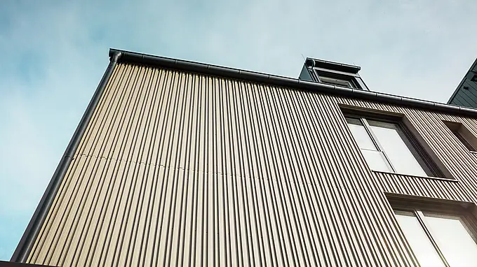 Na snímke je moderná budova vo Feldkirchene, ktorú navrhol architekt Stefan Heigl. Fasáda je obložená materiálom Prefalz vo farbe bronzová, zatiaľ čo šikmá strecha je pokrytá materiálom Prefalz v čiernošedej farbe. Veľké okná a strešné okná poskytujú v budove dostatok prirodzeného svetla. V návrhu sa spájajú vysokokvalitné materiály a elegantná architektúra, ktorá je funkčná aj estetická. Tento moderný spôsob výstavby a použitie materiálov Prefalz dodávajú budove moderný a štýlový vzhľad.