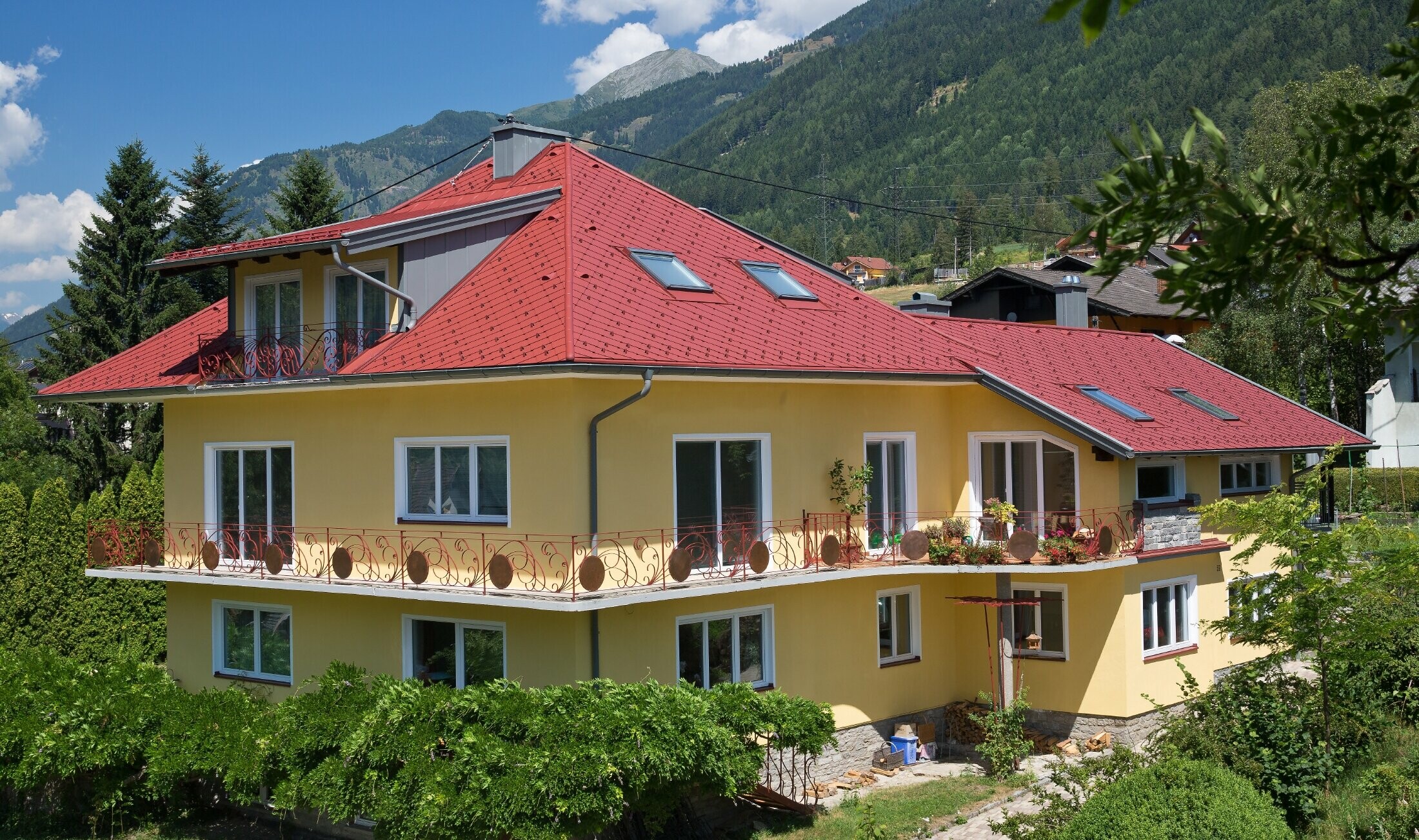 klasický rodinný dom s valbovou strechou obloženou strešnou šablónou tmavočervenej farby.