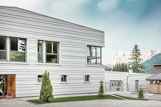 Detailný pohľad na kasárne „Tempesti“ s presne položenými pásmi PREFALZ v farbe P.10 prefa biela. Čisté línie horizontálne položeného stojatého falcového krytia zdôrazňujú moderný dizajn fasády. Svetlý povrch odráža slnečné svetlo a optimalizuje mikroklímu. V pozadí sa týčia impozantné hory Južného Tirolska – tu sa technika stretáva s prírodou na najvyššej úrovni.