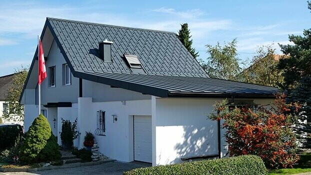 Zrekonštruovaný dom so sedlovou strechou a priľahlou garážou. Strecha domu bola pokrytá PREFA falcovanými škridlami a garáž krytinou Prefalz antracitovej farby. Pred domom je stožiar so švajčiarskou vlajkou. 