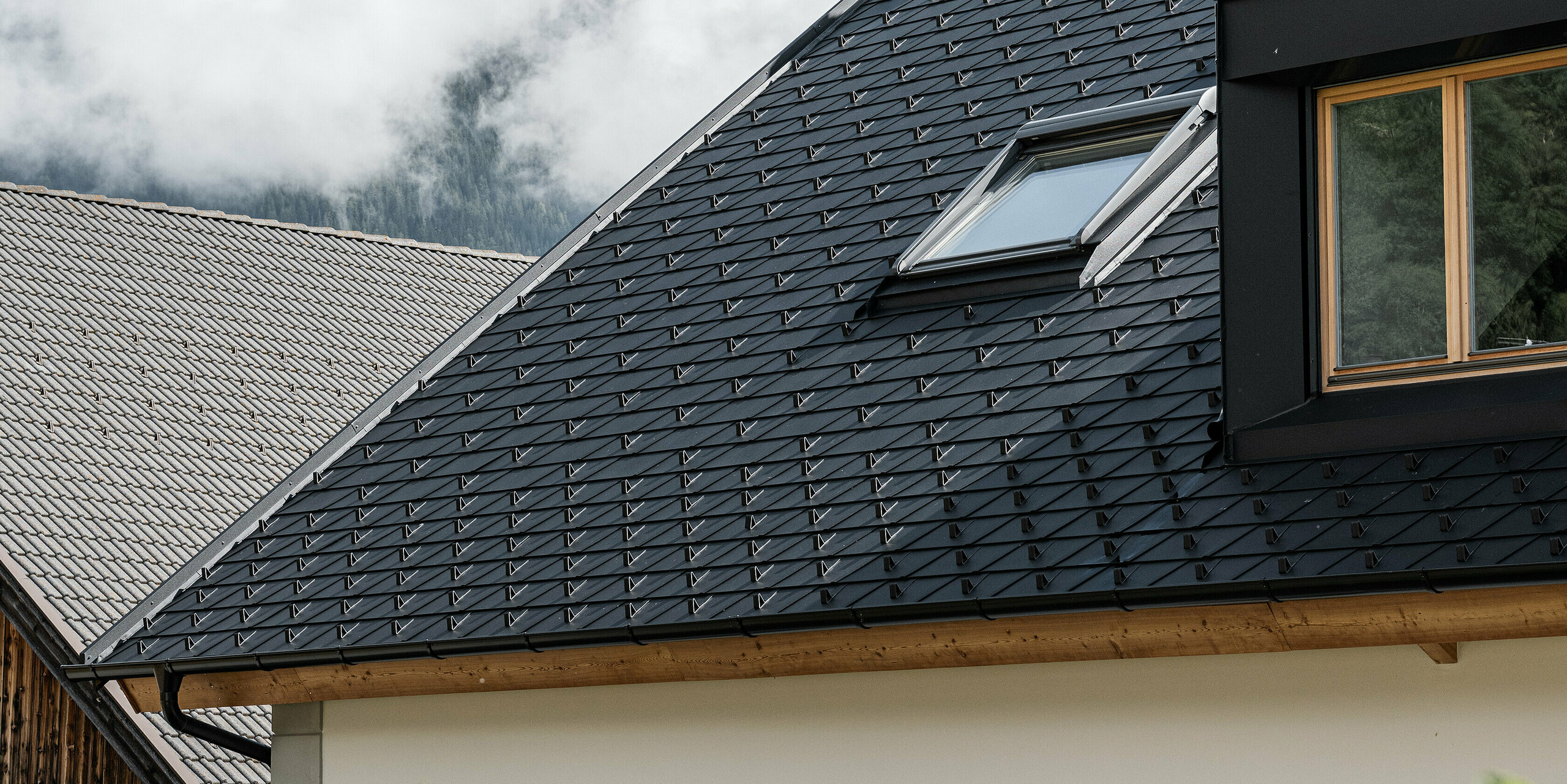 Detailný pohľad na strešný systém PREFA odolný voči vetru a poveternostným vplyvom. Sedlová strecha Ausserwegerhof v Južnom Tirolsku bola pokrytá robustnými strešnými šindľami PREFA DS.19 v antracitovej farbe P.10. Estetický dizajn strechy je obklopený pôsobivou horskou kulisou údolia Antholz.