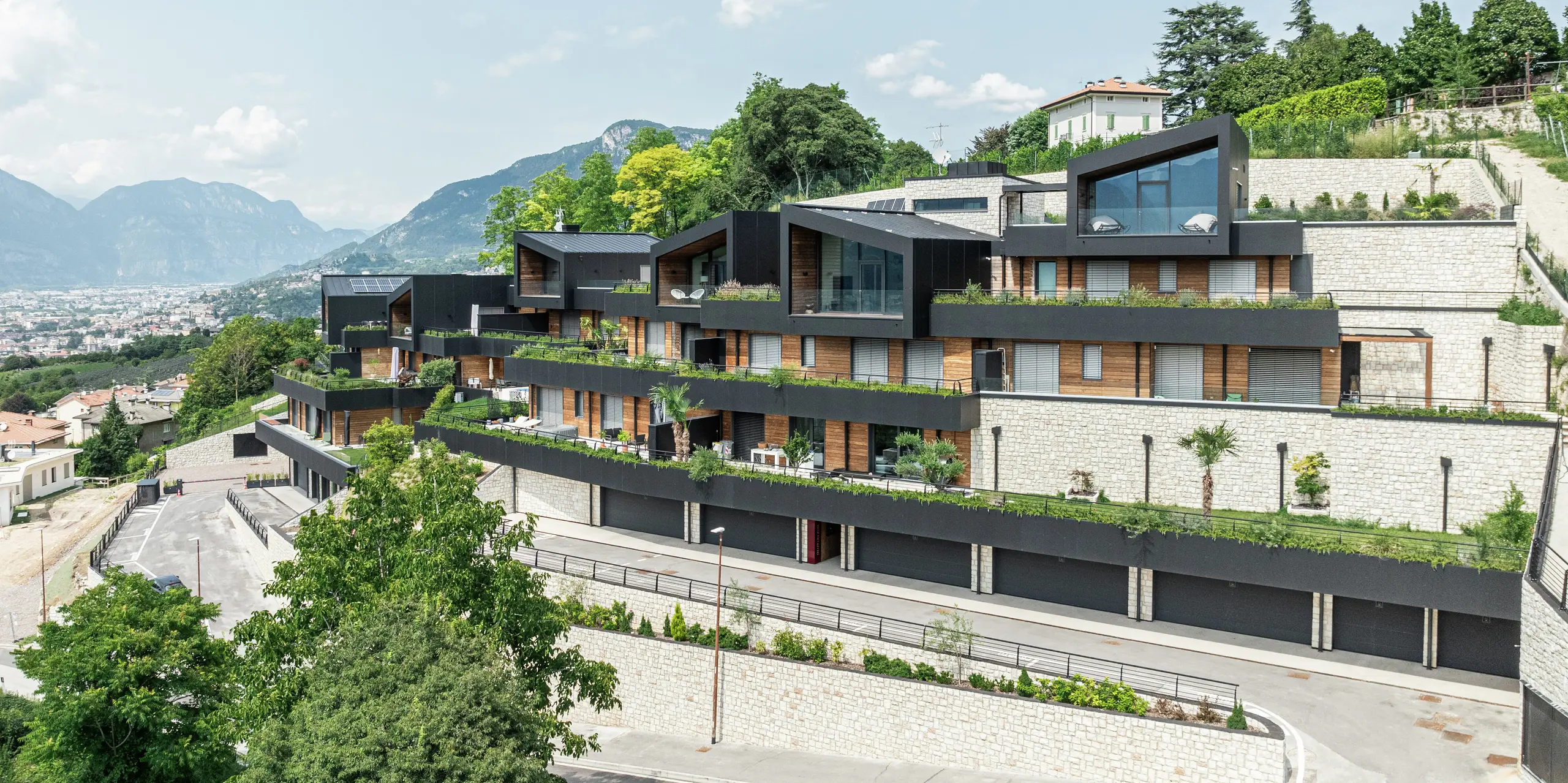 Obytný komplex sa dokonale začleňuje do svahov nad mestom Trento a ponúka impozantný panoramatický výhľad na mesto a okolité horské krajiny. Kombinácia prírodného kameňa, dreva a vysokokvalitnej hliníkovej fasády PREFA v čiernej farbe P.10 zaisťuje moderný, elegantný vzhľad s najvyššou odolnosťou voči poveternostným vplyvom. Strecha PREFALZ v čiernej farbe P.10 zaručuje dlhú životnosť a ochranu. Rozľahlé terasy s udržiavanou zeleňou podčiarkujú udržateľný koncept bývania a vytvárajú harmonické spojenie architektúry a prírody.