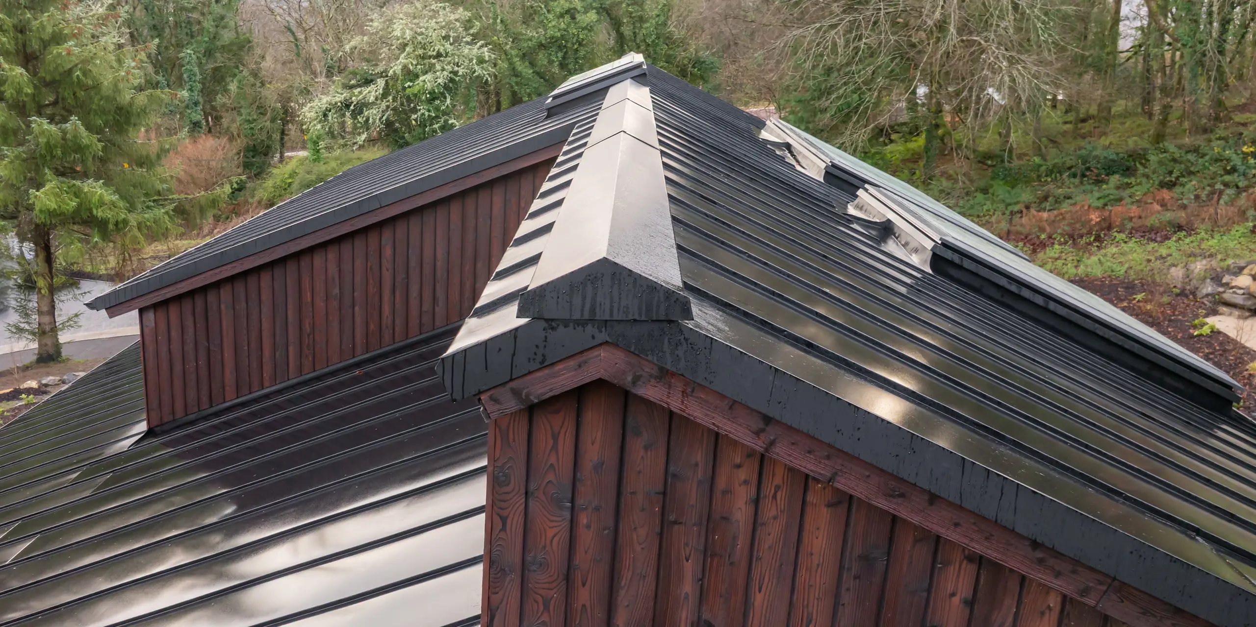Dynamische Perspektive über die Dachlandschaft des House of Holywell in Sligo: Das PREFALZ Aluminiumdach in P.10 Schwarz zieht sich präzise über geneigte Flächen und markante Firstlinien. Die stehenden Falze reflektieren das Licht und betonen die Geometrie der Architektur. Sichtbare Details wie Grat- und Firstausbildung unterstreichen die handwerkliche Qualität. Das PREFA Dach überzeugt durch Langlebigkeit, Korrosionsbeständigkeit und zuverlässigen Schutz bei jeder Witterung.