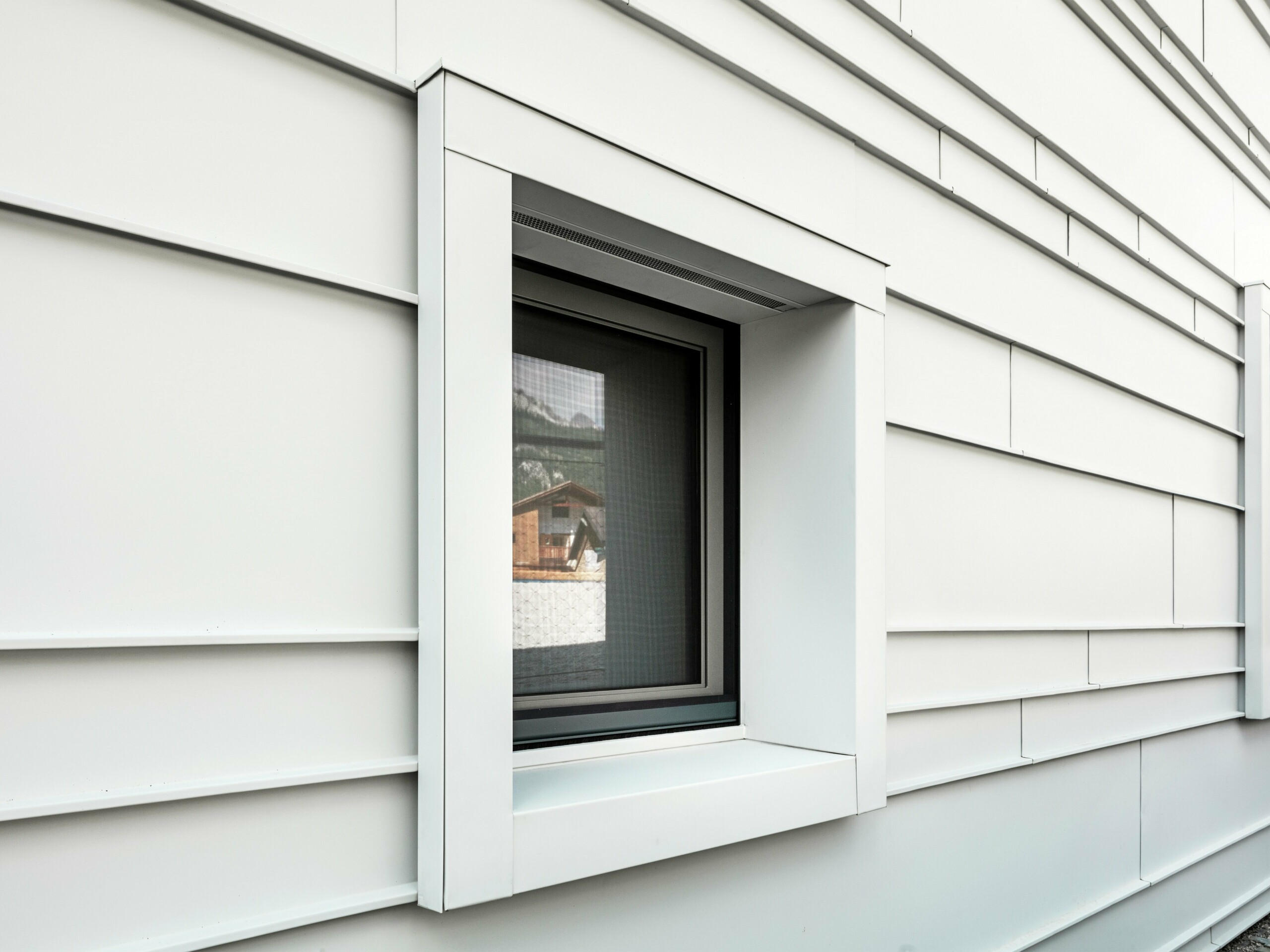 Detailný záber výrazných okenných výrezov v odvetranej fasáde z PREFALZ P.10 vo farbe prefa biela. Horizontálne položené hliníkové plechy dodávajú štruktúru, prehľadnosť a moderný vzhľad. Výrazné okenné rámy kasární „Tempesti” začínajú a končia vždy presne na línii ohybu. Tým sa zámerne zdôrazňuje štruktúra hliníka.