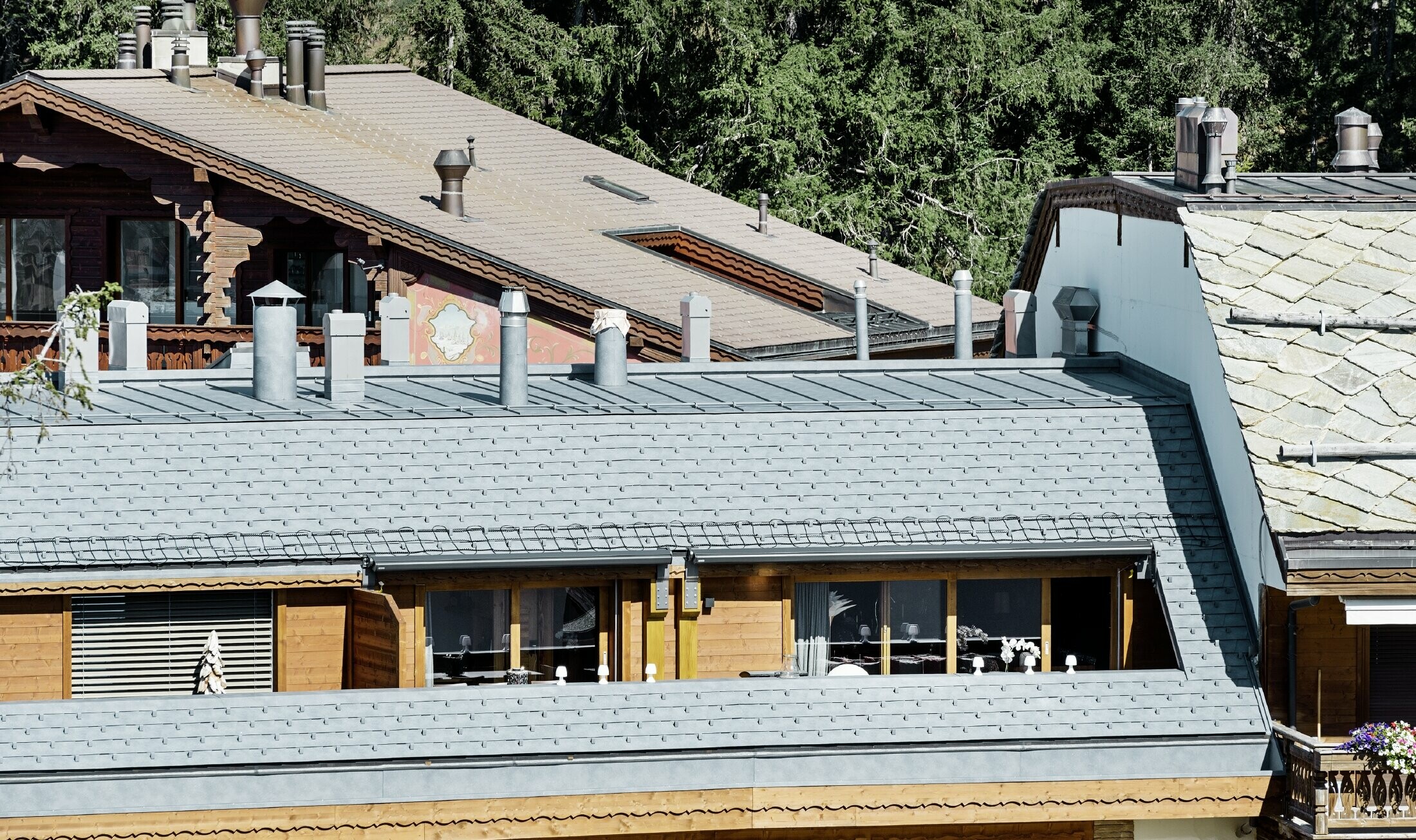 Bytový dom v Crans-Montane s horami v pozadí s fasádou s hravými drevenými prvkami a hliníkovou šindľovou strechou PREFA vo farbe kamenná šedá