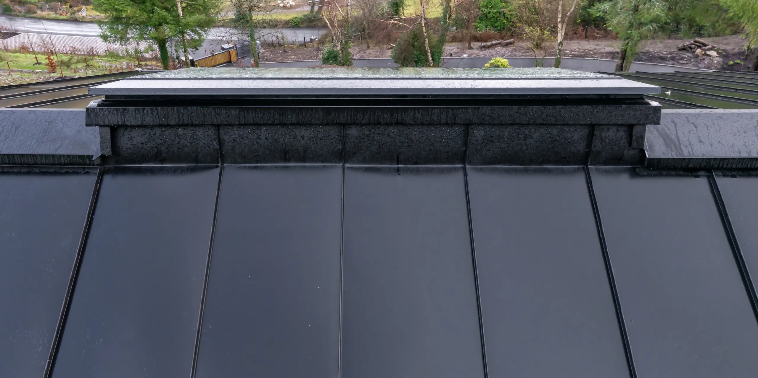 Markante Perspektive entlang des Dachfirsts beim House of Holywell in Sligo: Die präzisen Linien des PREFALZ Aluminiumdachs in P.10 Schwarz führen den Blick über die gleichmäßig rhythmischen Stehfalze bis in die weite Landschaft. Die detailgenaue Firstausbildung und sauberen Anschlüsse zeigen die hohe Verarbeitungsqualität. Die glatte Oberfläche lässt Regenwasser effizient ablaufen und unterstreicht die Vorteile des PREFA Dachs – langlebig, korrosionsbeständig und optimal für anspruchsvolle Witterungsbedingungen.