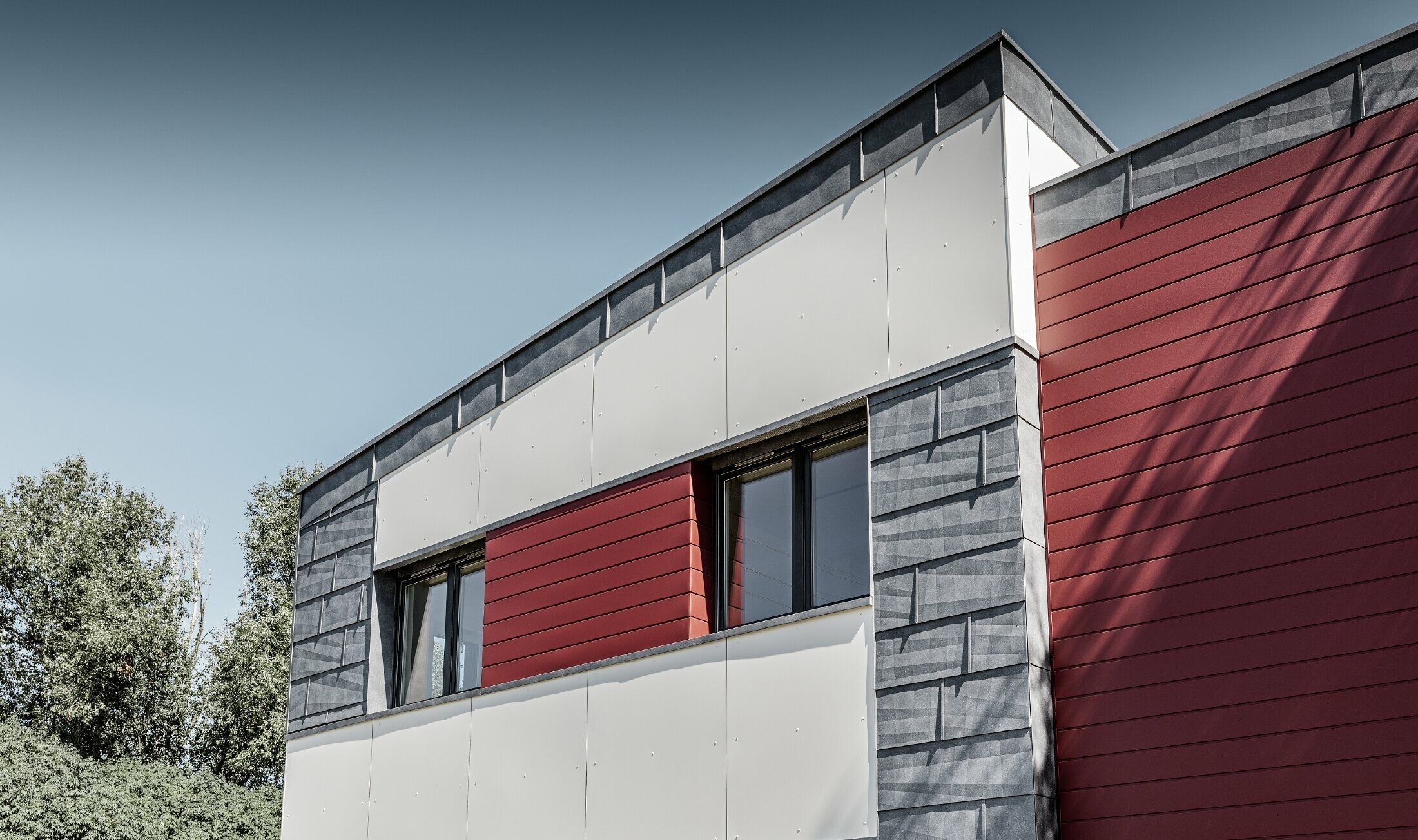 Moderná kancelárska budova s delenou hliníkovou fasádou vytvorenou z PREFA Siding v červenej, kamennošedej a bielej farbe, z PREFA fasádneho panelu FX.12 a z PREFA hliníkového kompozitného panela