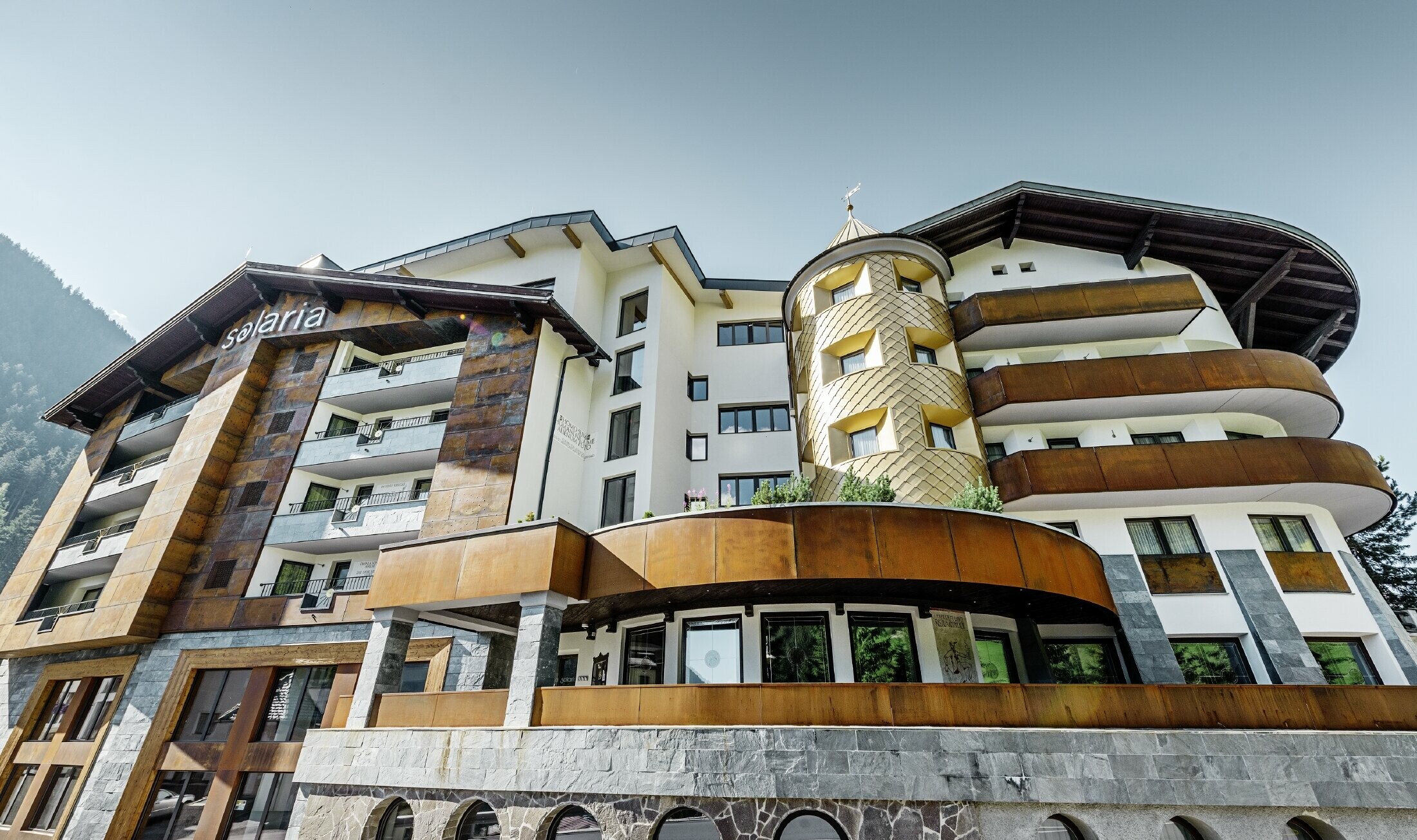 Tradičný hotel v Ischgl-e s drevenými balkónmi a drevenou fasádou a vežou so zlatými hliníkovými šablónami od firmy PREFA