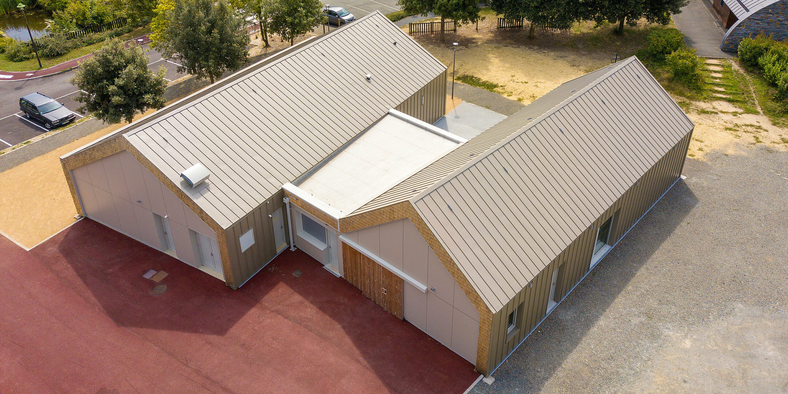 Pohľad z vtáčej perspektívy na mládežnícke centrum Salles Espace Bellevue v Mûrs-Erigné, Francúzsko. Obe budovy sú vybavené obkladom so stojatou drážkou z materiálu PREFALZ v bronzovej farbe. Hliníkový obklad PREFA odolný voči poveternostným vplyvom a s dlhou životnosťou ponúka moderné a udržateľné riešenie pre architektonicky náročné projekty.