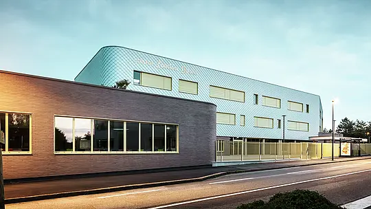 Večerný pohľad na Collège Léontine Dolivet v Cesson-Sévigné. V popredí vedie jasne vyznačená ulica, vedľa nej sa nachádza plochá časť budovy s veľkými sklenenými oknami. Za ňou sa týči hlavná budova so zakrivenou hliníkovou fasádou z PREFA fasádnych šablón v striebornom metalickom vyhotovení, ktoré sa mení v jemnom svetle. Niekoľko obdĺžnikových okien a svetlý plot dotvárajú celkový pohľad. Scénu osvetľujú pouličné lampy, obloha má chladnú modrú farbu – moderný, elegantný pohľad.