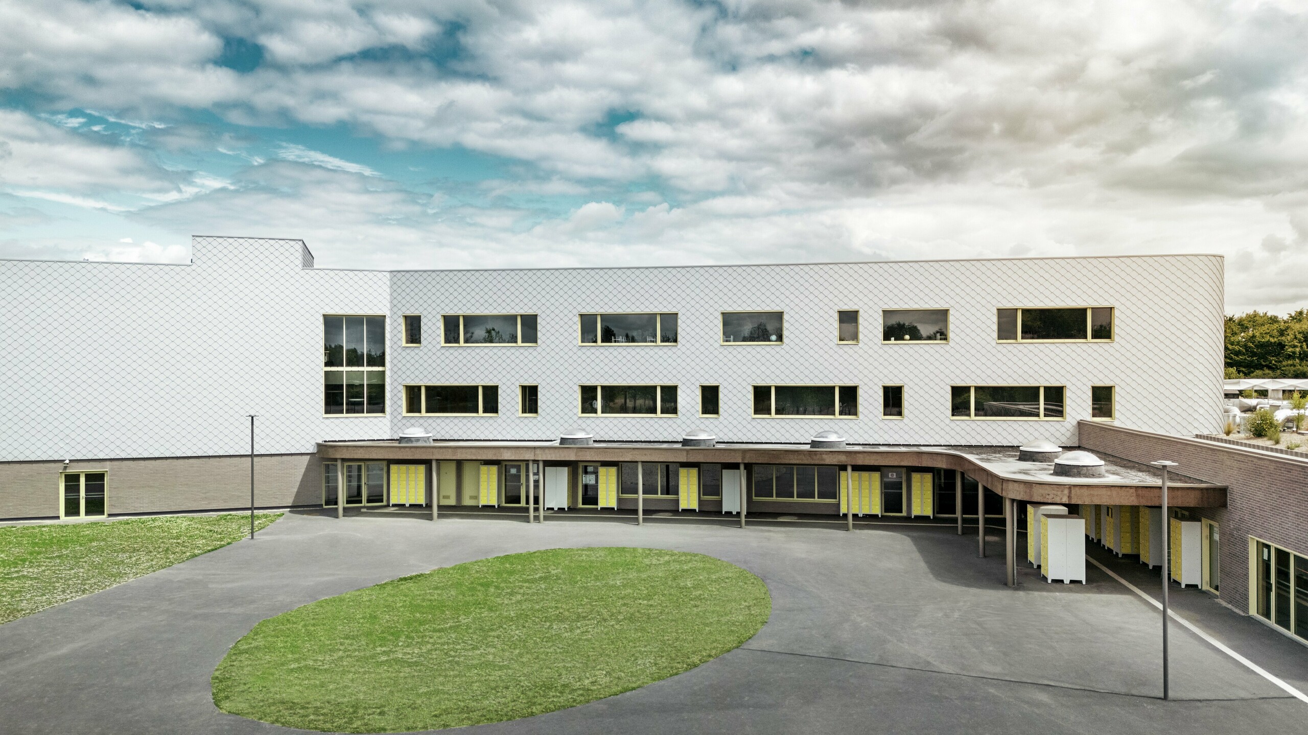 Zadná strana školy Collège Léontine Dolivet s veľkým školským dvorom a čistou architektúrou. Fasáda je tvorená striebornými kovovými fasádnymi šablónami PREFA, ktoré jej dodávajú moderný, elegantný vzhľad. Niekoľko radov okien a žlté dvere oživujú štruktúru, zatiaľ čo asfaltové nádvorie s centrálnou zelenou plochou ponúka veľa priestoru na prestávky. Odolná hliníková fasáda kombinuje ľahkosť, odolnosť voči poveternostným vplyvom a dizajn – funkčný a estetický pohľad v Cesson-Sévigné neďaleko Rennes.