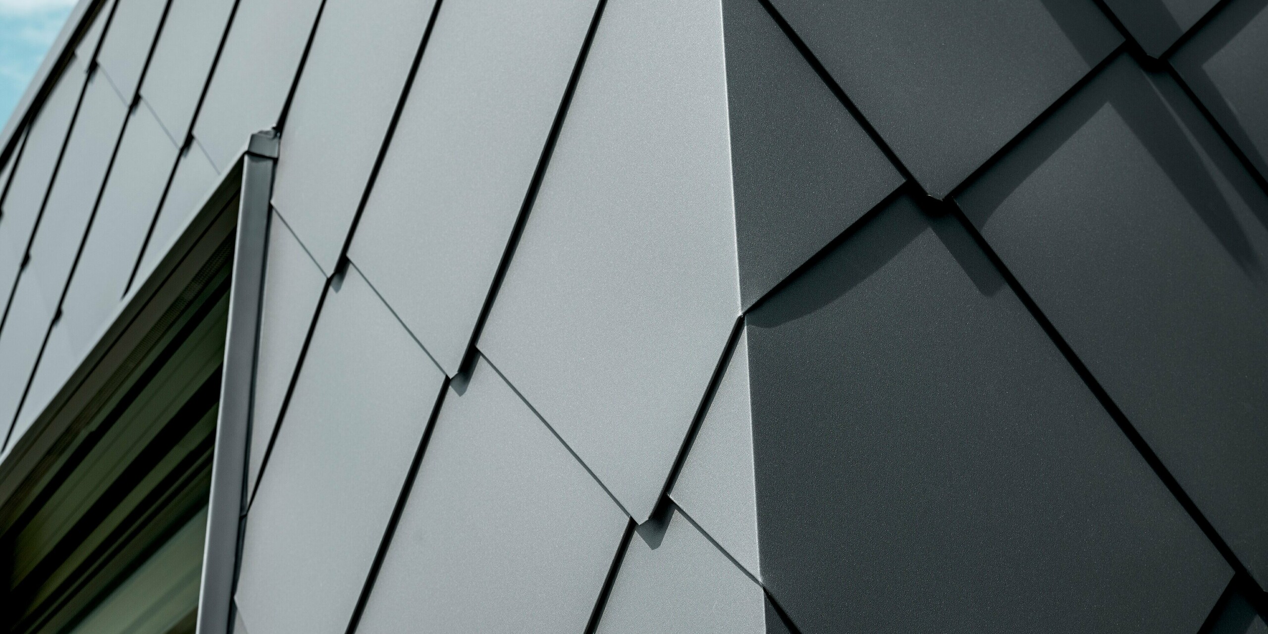 Detailný záber na strešné a fasádne šablóny PREFA 44 × 44 v odtieni P.10 tmavošedá na rodinnom dome v Trnave. Na obrázku je vidieť precízne položenú štruktúru šablón, ktorých čisté línie a hrany zvlášť zdôrazňujú vysokú kvalitu hliníka. Matný povrch zaisťuje elegantné odrazy svetla a dodáva fasáde moderný, technický vzhľad. Odolné hliníkové produkty PREFA ponúkajú maximálnu odolnosť voči poveternostným vplyvom, stabilitu a jednotný vzhľad pre výraznú, nadčasovú architektúru.