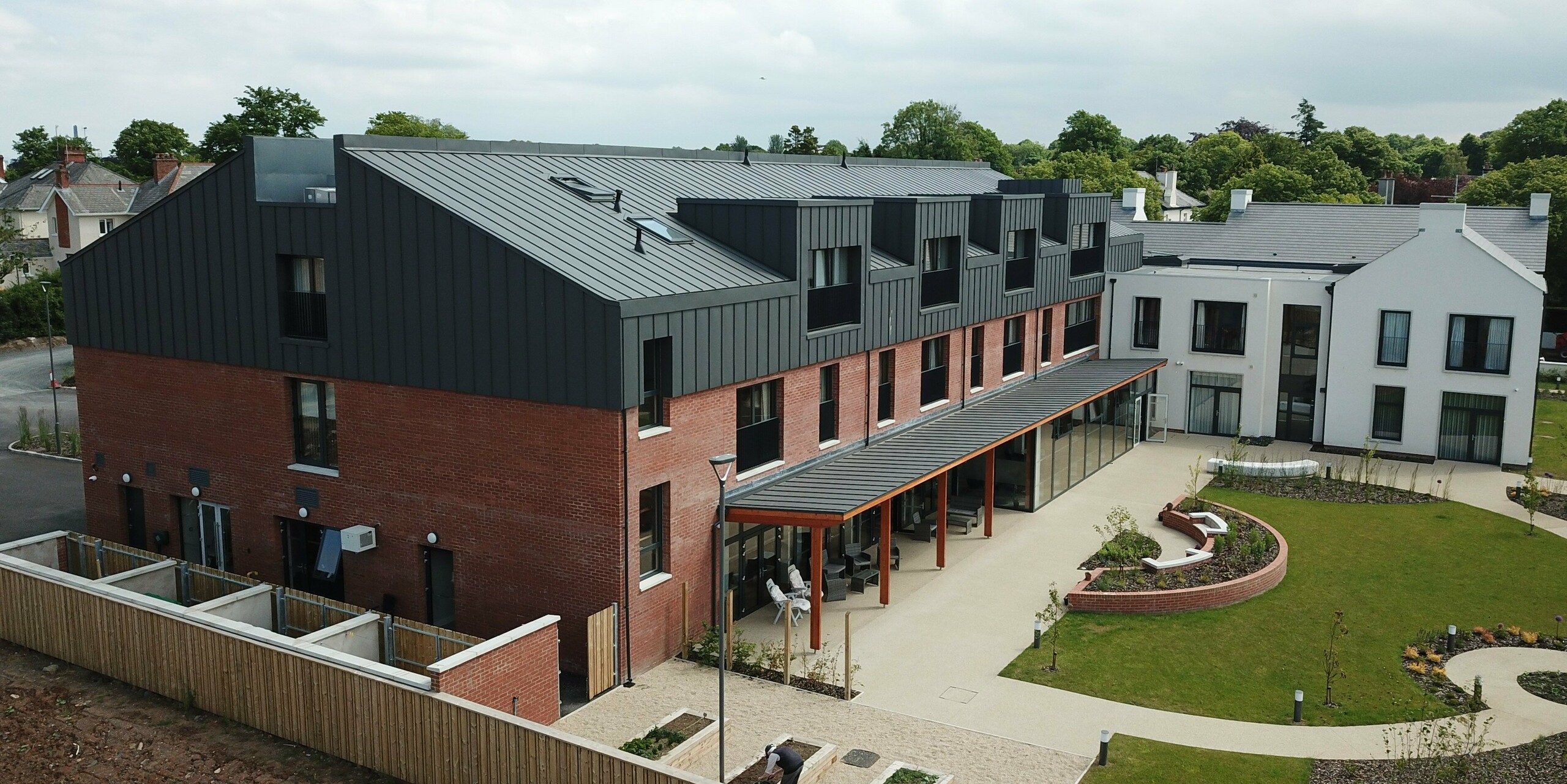 Seitenansicht der Harberton Hall mit Klinkerfassade und PREFALZ Aluminiumverkleidung in P.10 Dunkelgrau. Die Flachdachgauben und der moderne Materialmix sorgen für ein zeitloses Erscheinungsbild. Das Gebäude für betreutes Wohnen vereint Nachhaltigkeit, Funktionalität und elegantes Design.