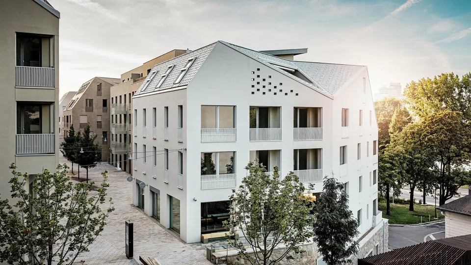 Moderná obytná štvrť Vydrica v Bratislave sa vyznačuje jasným architektonickým jazykom a pokojnou atmosférou uličiek. Strmé sedlové strechy s výraznými strešnými oknami sú pokryté hliníkovými strešnými šindľami PREFA vo farbách P.10 prefa biela, bronzová a P.10 pieskovo hnedá, ktoré na slnku vytvárajú elegantný vizuálny akcent. Precízne vyhotovené línie a homogénne plochy podčiarkujú vysokú kvalitu architektonického riešenia. Hliník PREFA presviedča dlhou životnosťou, nízkou hmotnosťou a vysokou odolnosťou voči poveternostným vplyvom – ideálne riešenie pre zložité tvary striech a udržateľný, nenáročný obvodový plášť budovy.