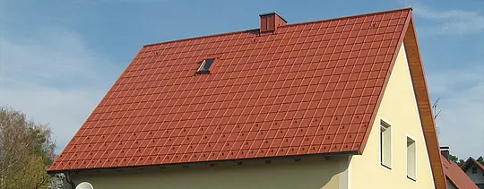 Klasická sedlová strecha s malým strešným oknom a komínom, pokrytá PREFA škridlou v tehlovočervenej farbe vrátane snehových zábran a strešných bezpečnostných hákov.