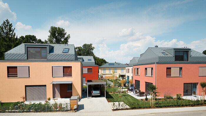 Bytový dom s fasádami v odtieňoch červenej a s hliníkovými šablónovými strechami PREFA svetlošedej farby