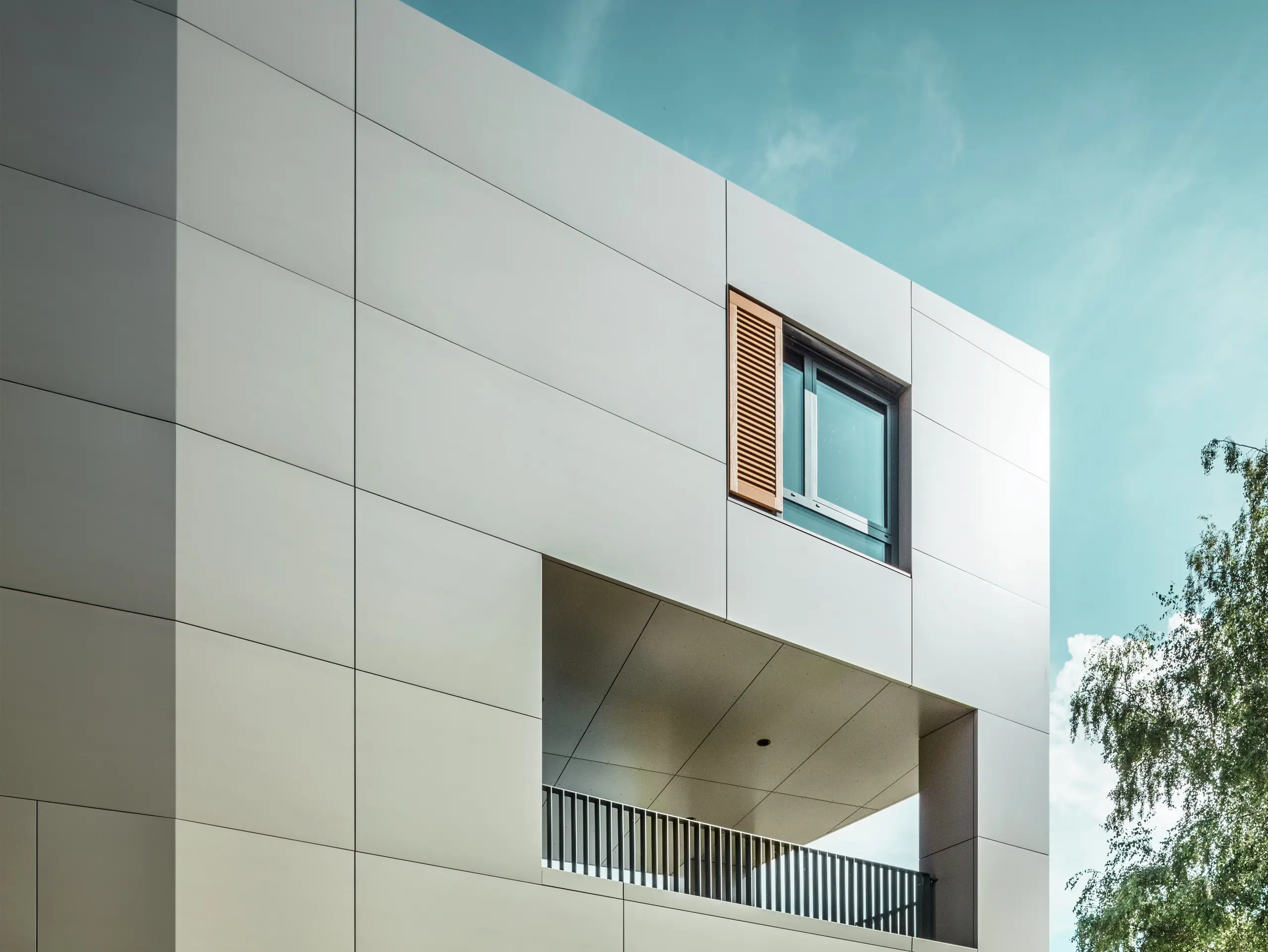 Na obrázku je moderná radnica v Alzenau s fasádou z hliníkových kompozitných panelov PREFA v bronzovej farbe. Architektúra sa vyznačuje jasnými geometrickými tvarmi a veľkými oknami. Špicatá strecha a decentné osvetlenie dodávajú budove elegantný, moderný vzhľad.
