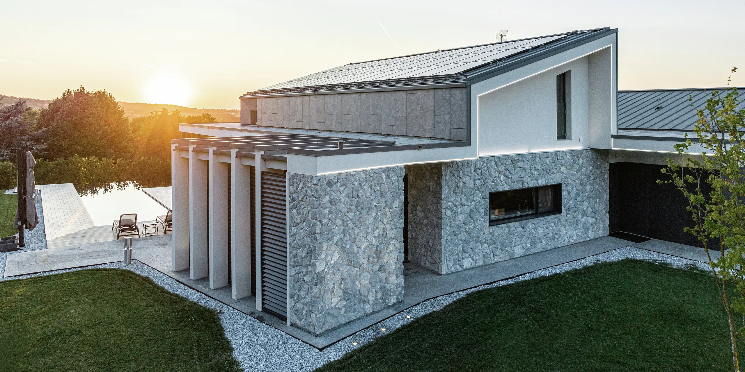 Detailný pohľad na luxusný rodinný dom v Scandiano, Taliansko. Strešné plochy z PREFALZu vo farbe P.10 antracit poskytujú moderný, elegantný vzhľad a optimálnu ochranu pred poveternostnými vplyvmi. Fasáda z prírodného kameňa a čisté línie dizajnu dokonale harmonizujú s vysokokvalitným riešením strechy PREFA a sofistikovanou architektúrou.