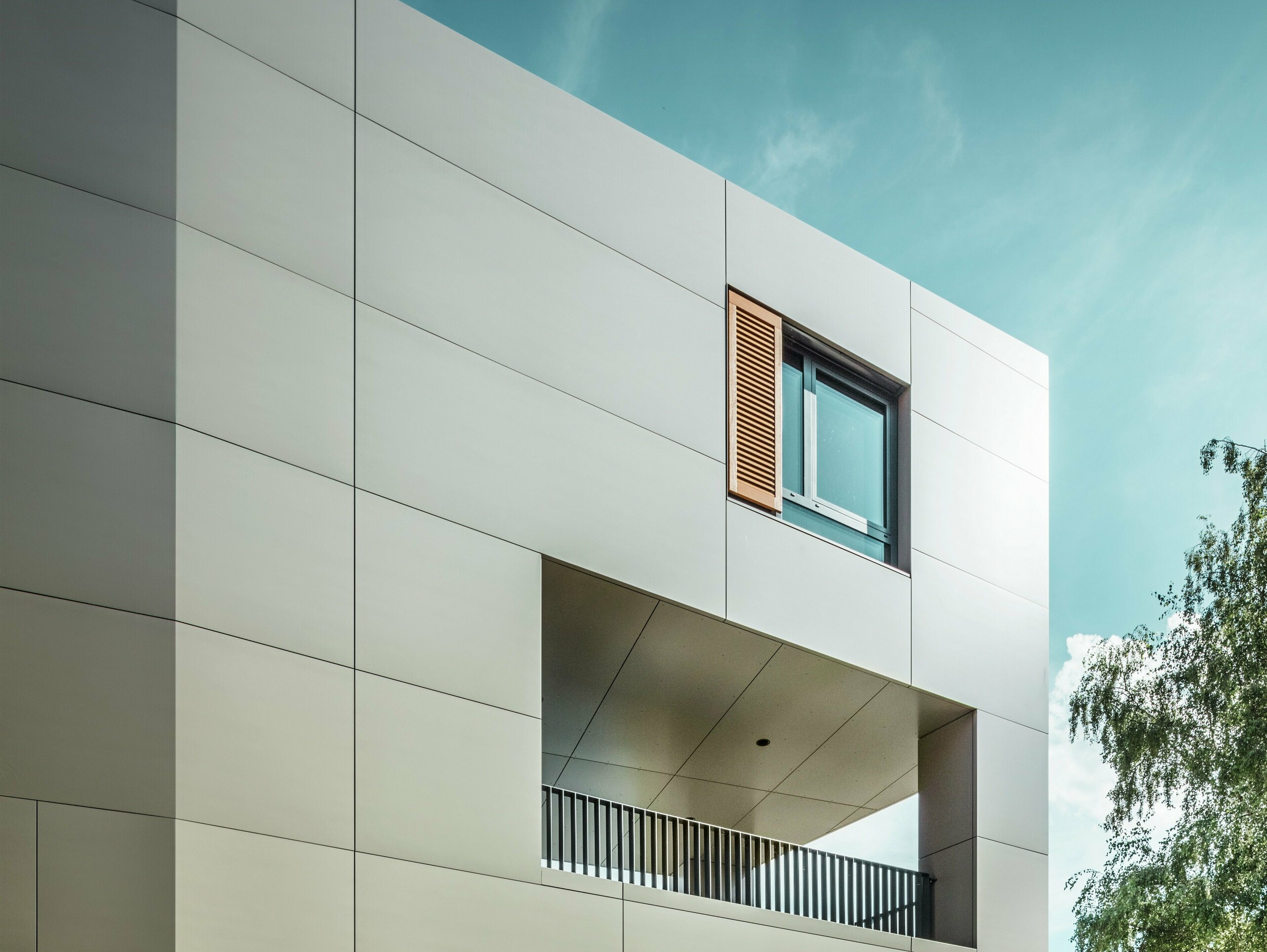 Na obrázku je moderná radnica v Alzenau s fasádou z hliníkových kompozitných panelov PREFA v bronzovej farbe. Architektúra sa vyznačuje jasnými geometrickými tvarmi a veľkými oknami. Špicatá strecha a decentné osvetlenie dodávajú budove elegantný, moderný vzhľad.