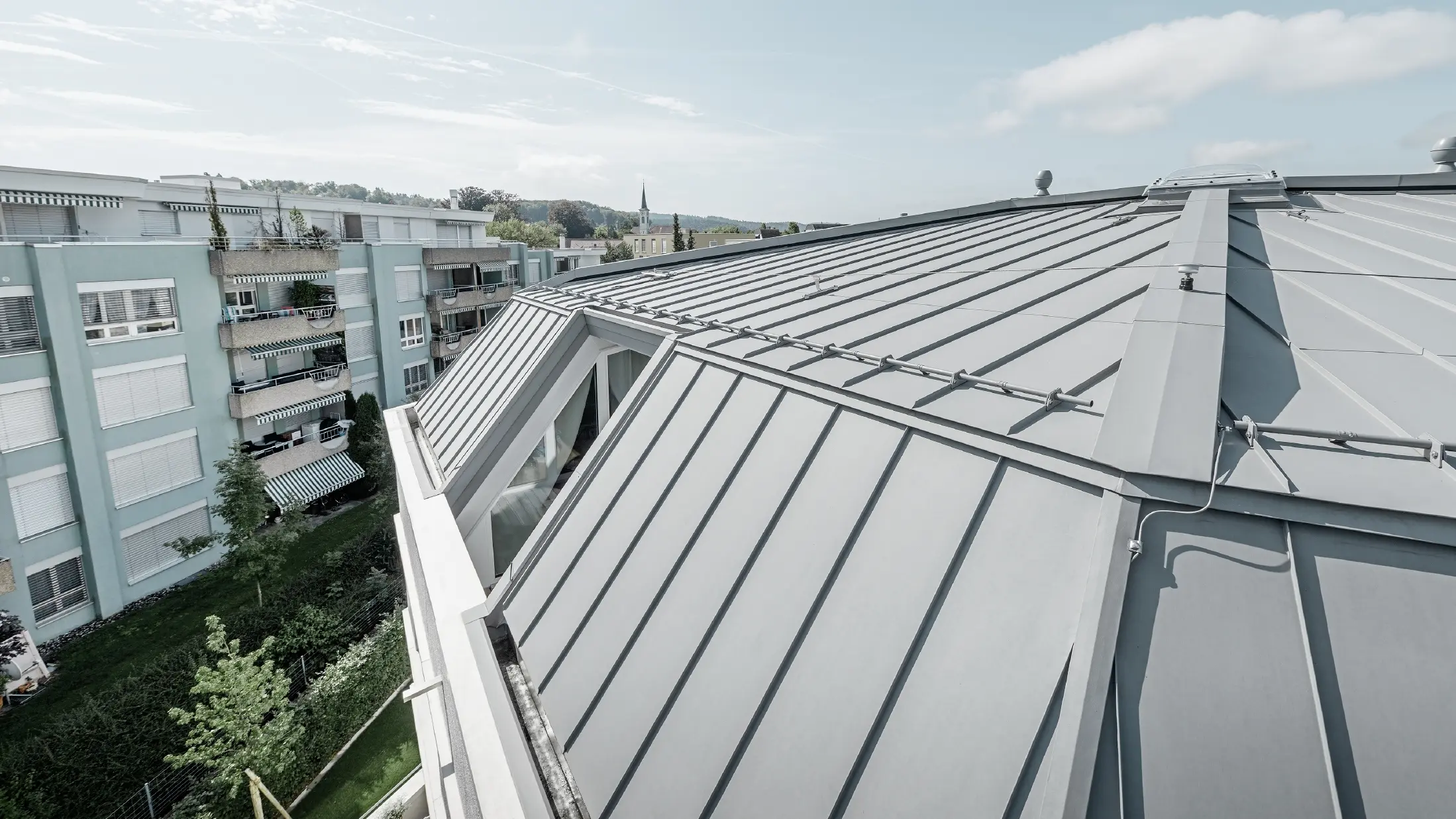 Detailný pohľad na povrch strechy bytového domu; strecha so stojatou drážkou s povrchovou úpravou PREFA Prefalz vo farbe patina šedá