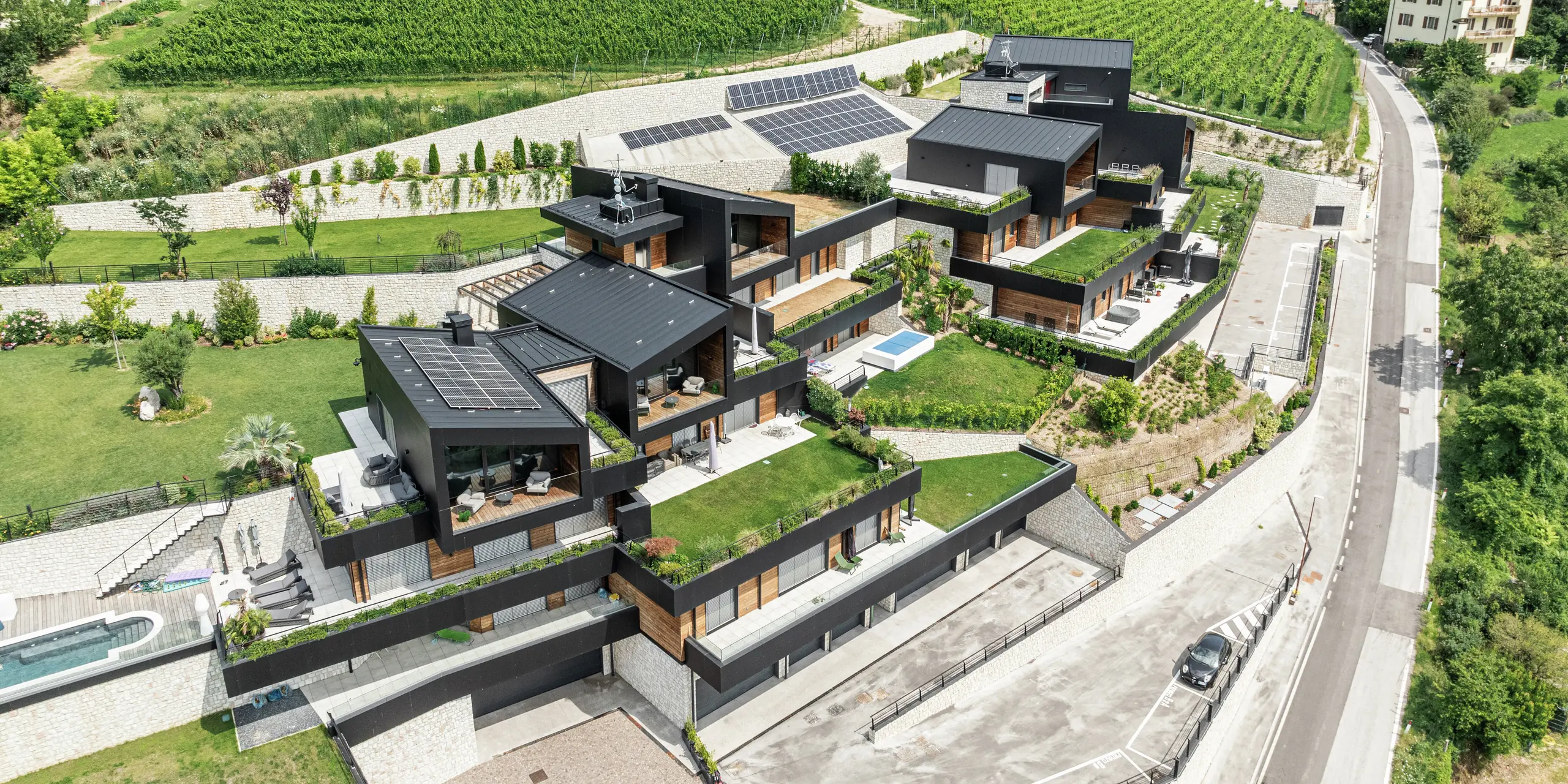 Tento exkluzívny rezidenčný komplex, zasadený do malebnej kopcovitej krajiny Trenta, spája udržateľnú výstavbu s moderným dizajnom. Fasády z hliníkových kompozitných dosiek PREFA v čiernej farbe P.10 a strechy z PREFALZ poskytujú najvyššiu ochranu pred poveternostnými vplyvmi a zaisťujú elegantný a trvalý vzhľad. Priestranné terasy, starostlivo udržiavaná zeleň a fotovoltaické systémy podčiarkujú ekologický koncept. Harmonické začlenenie do prírody a luxusné detaily, ako sú súkromné bazény a udržiavané záhrady, robia z tohto rezidenčného projektu jedinečné miesto pre pohodu a relax.