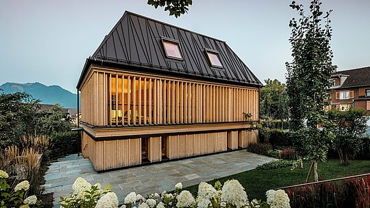 Moderný „kúpeľný dom“ v hoteli Hirschen v Schwarzenbergu má strechu PREFA so stojatými falcami vo farbe P.10 orieškovohnedá. Ikona valbová strecha so sklonom 60 stupňov a netradične umiestnenými stojatými falcami je architektonickým vrcholom, ktorý spája tradíciu a inováciu. Fasáda z vertikálnych drevených lamiel dodáva budove teplý, prirodzený vzhľad a harmonicky zapadá do pamiatkovo chráneného centra mesta. PREFALZ presviedča svojou dlhou životnosťou, voľnosťou tvarov a vynikajúcou spracovateľnosťou, aj pri zložitých tvaroch striech. Ocenený príklad inovatívnej architektúry s vysokokvalitnými produktmi PREFA