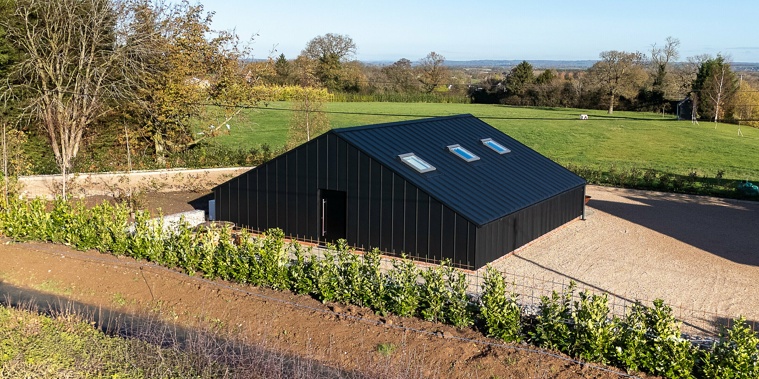 Rückansicht des modernen Freizeitgebäudes mit vollständig verkleideter PREFA Aluminiumfassade und PREFALZ Dachfläche in P.10 Schwarz. Die klare, geometrische Form und die homogene Aluminiumoberfläche setzen einen architektonischen Kontrast zur umliegenden Landschaft. Die witterungsbeständige, langlebige Ausführung bietet maximalen Schutz und hochwertige Optik im Außenbereich.